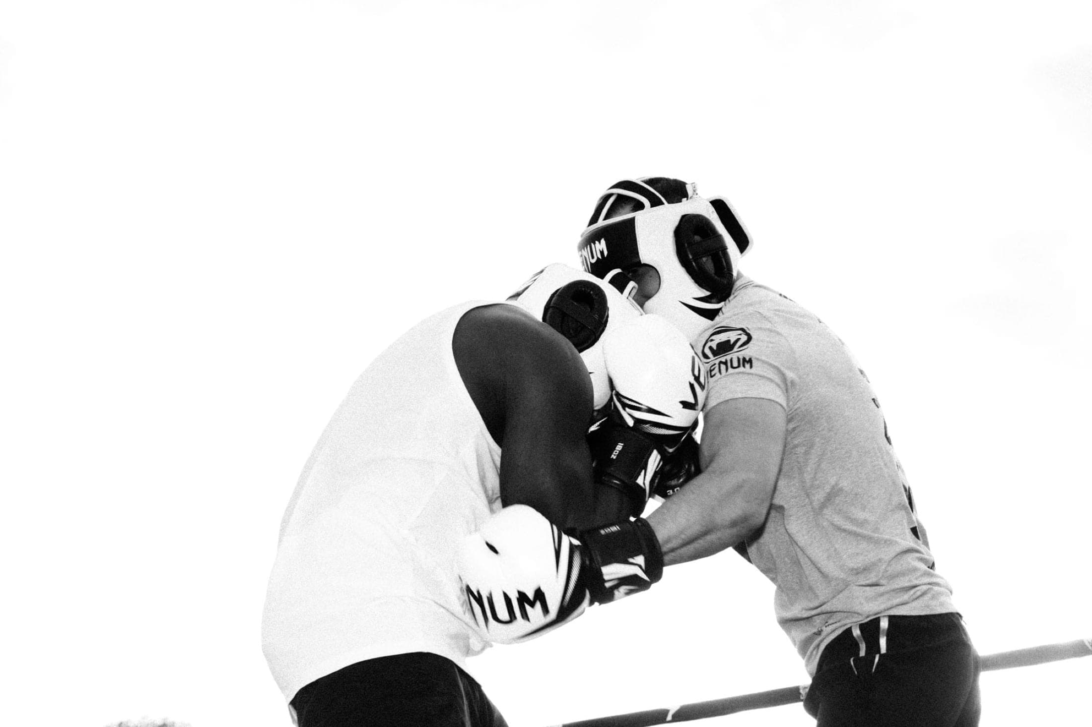 Noir et blanc : front contre front dans le corps à corps, les gants serrés entre les deux torses, ciel blanc.