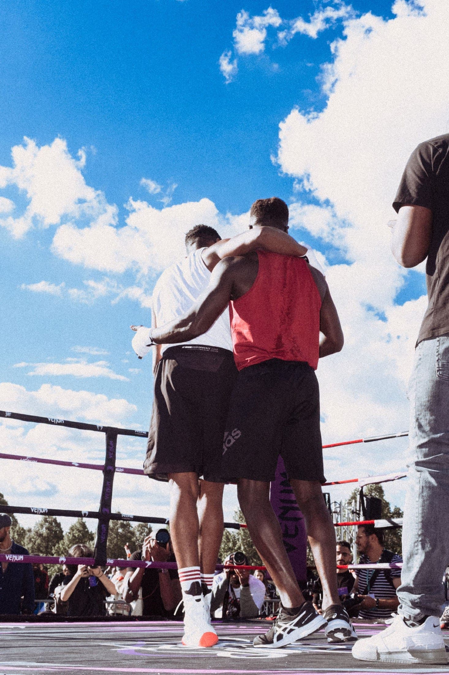 Après le combat, les deux boxeurs s'étreignent bras autour des épaules, vus de dos face au public.