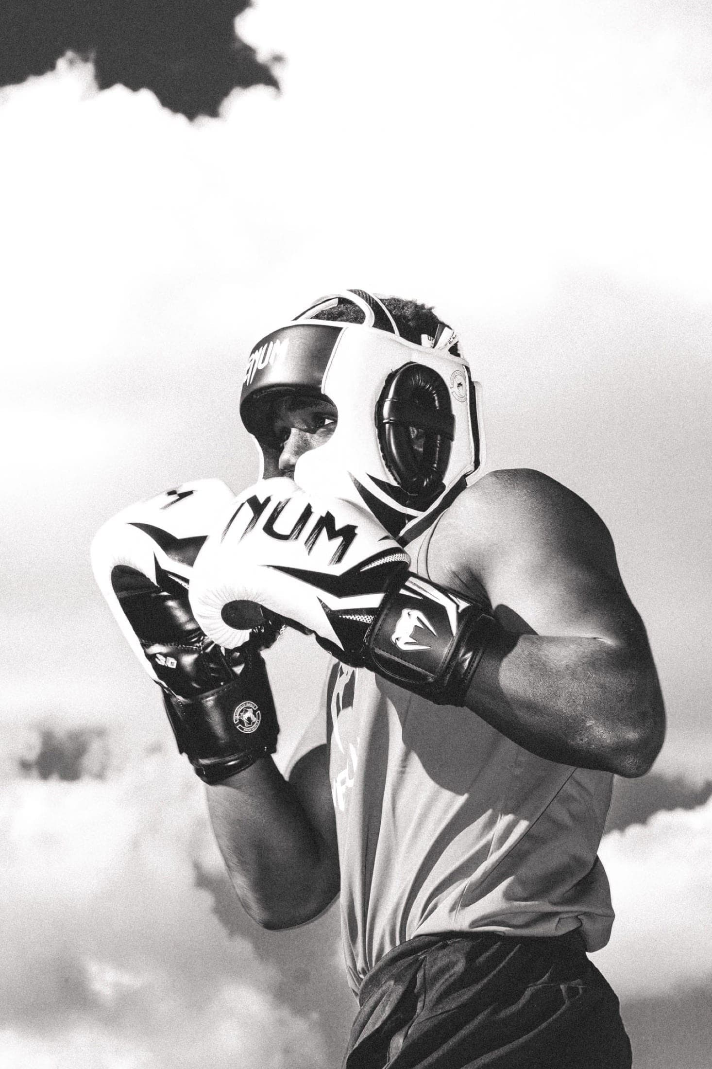 Noir et blanc : portrait en garde, casque et gants relevés devant le visage, ciel nuageux derrière.