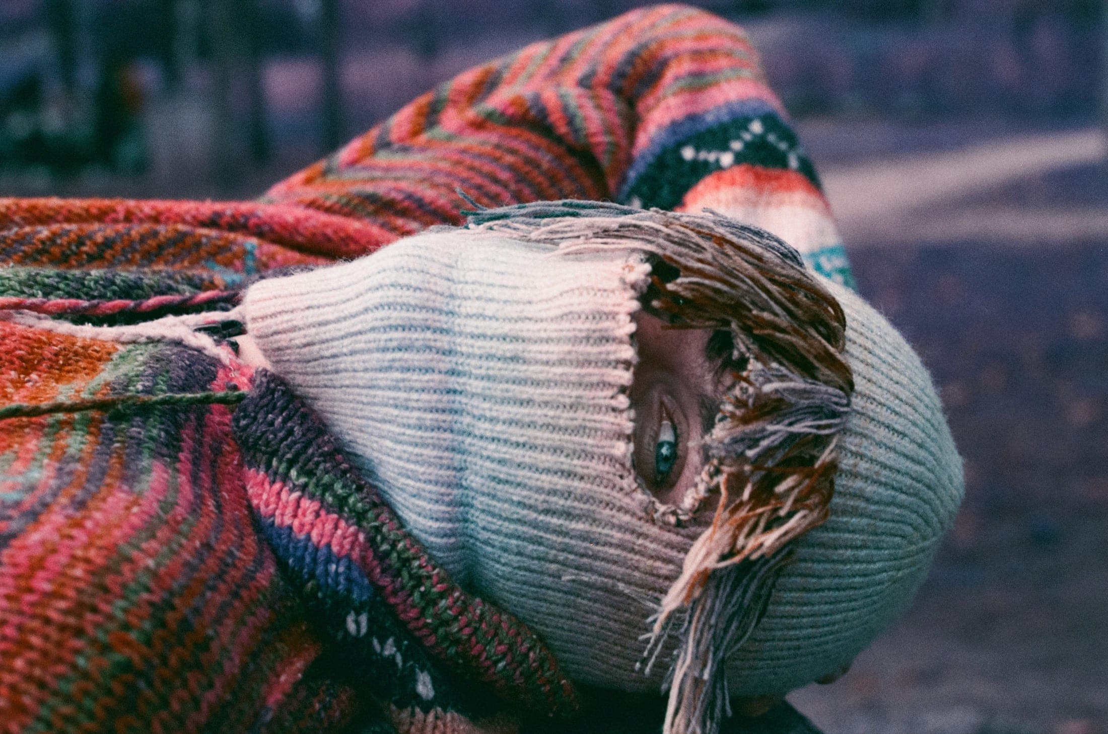 Gros plan sur un visage allongé, un œil bleu visible dans la déchirure de la cagoule, entouré de mailles multicolores.