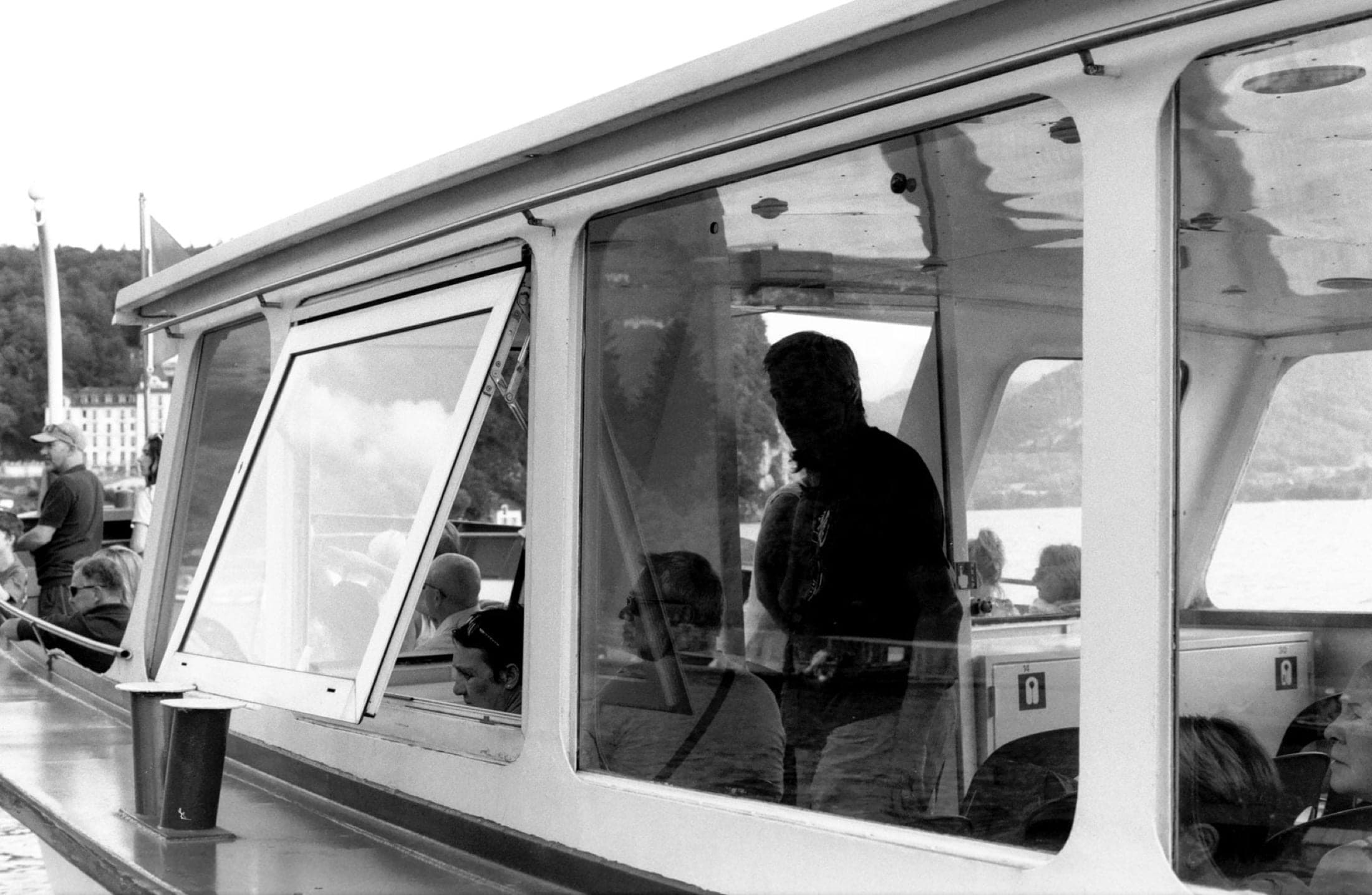 Passagers derrière les vitres d'un bateau de ligne, un membre d'équipage debout dans la cabine.