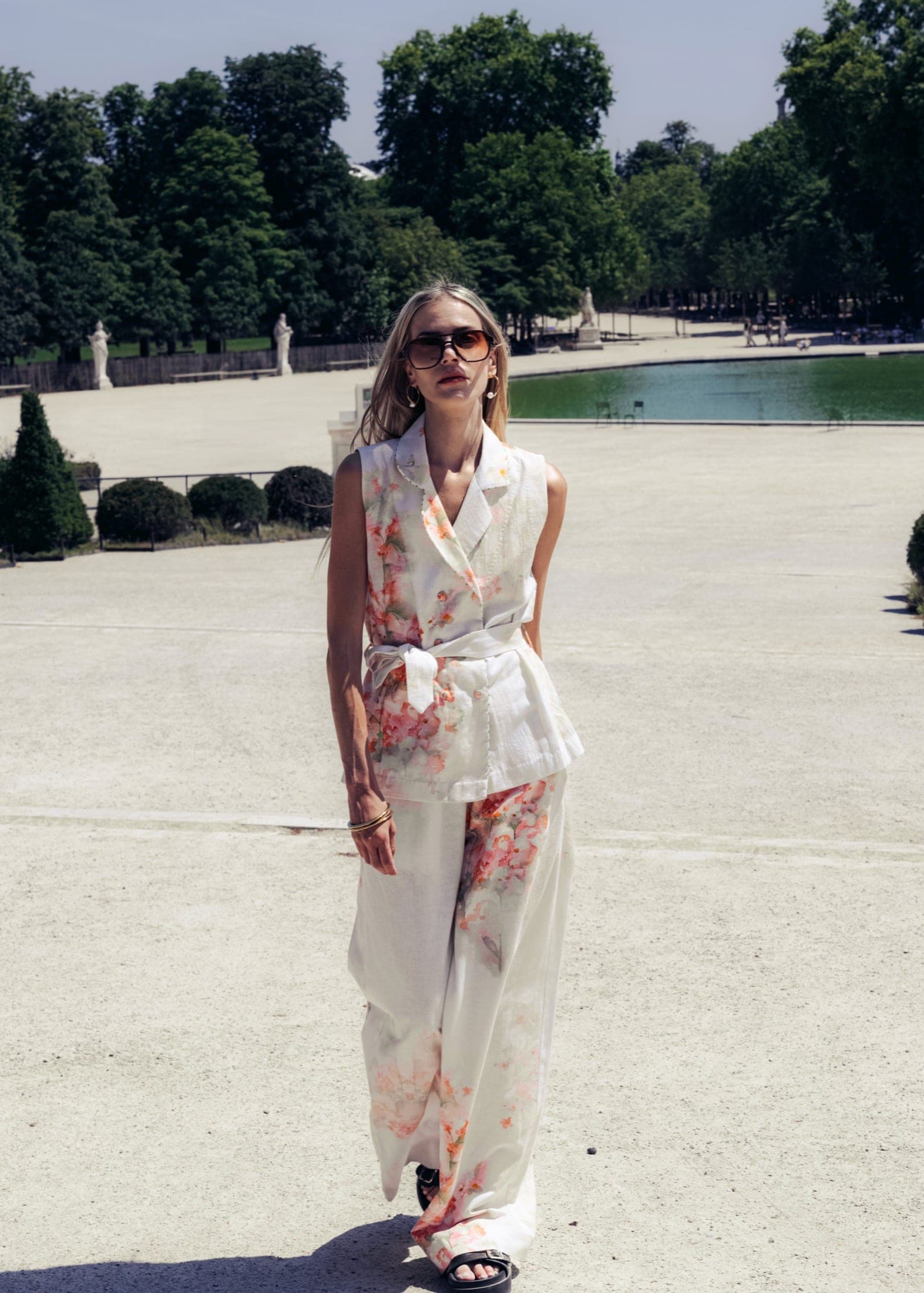 Ensemble gilet cintré et pantalon large à fleurs pêche, lunettes aviateur, devant le grand bassin des Tuileries.