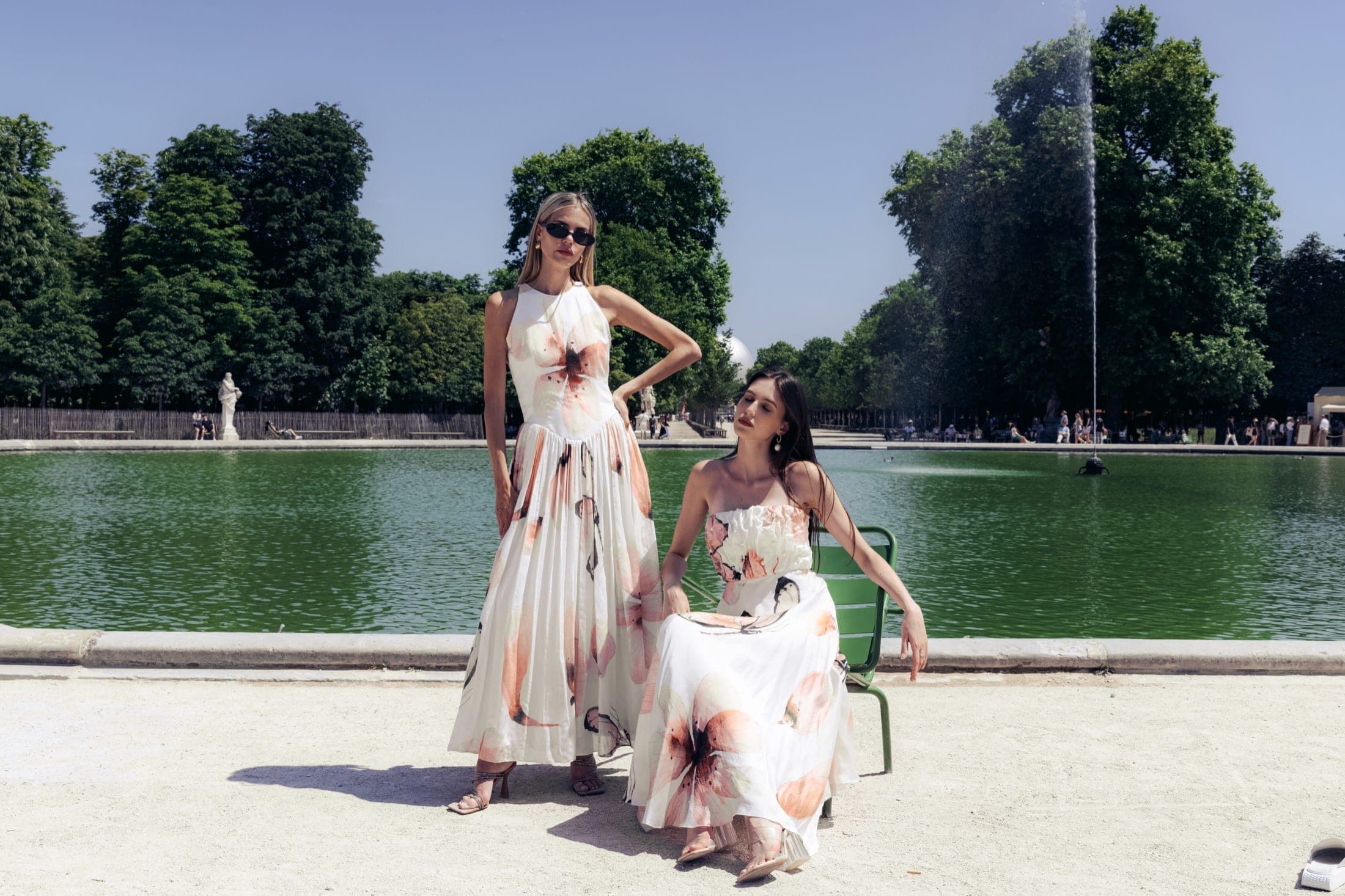 Deux mannequins près du bassin des Tuileries, l'une debout en robe florale hanche cassée, l'autre assise sur une chaise verte en bustier perlé.
