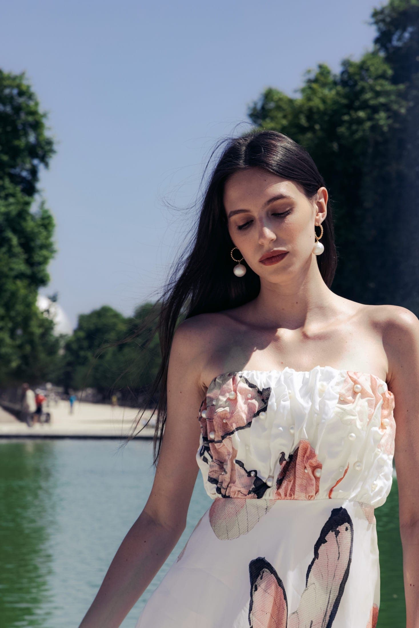 Bustier perlé à motif papillon en gros plan, le menton posé sur la main, boucles d'oreilles perle et or.