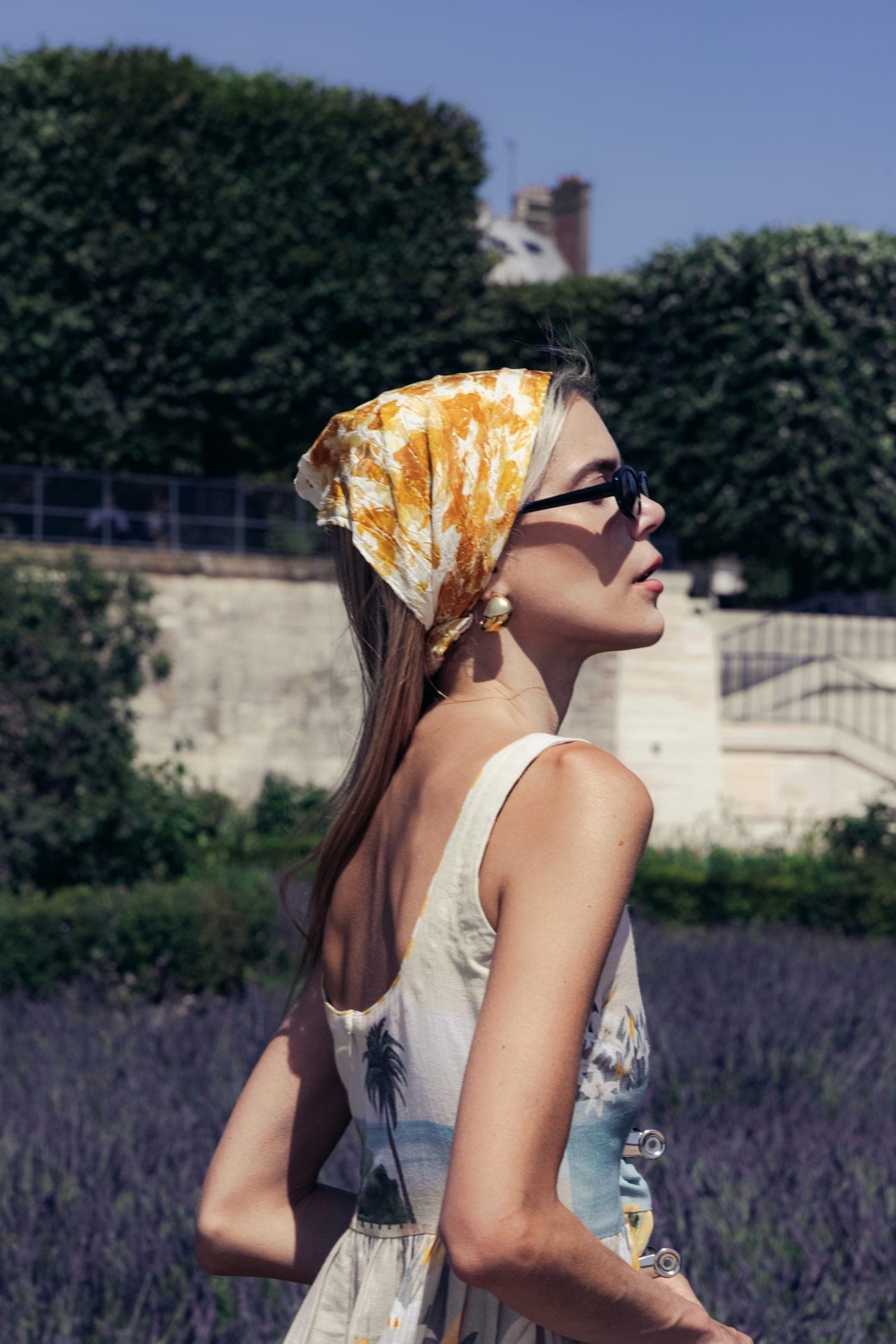 Foulard jaune noué et lunettes de soleil rondes en profil serré, boucle d'oreille dorée.