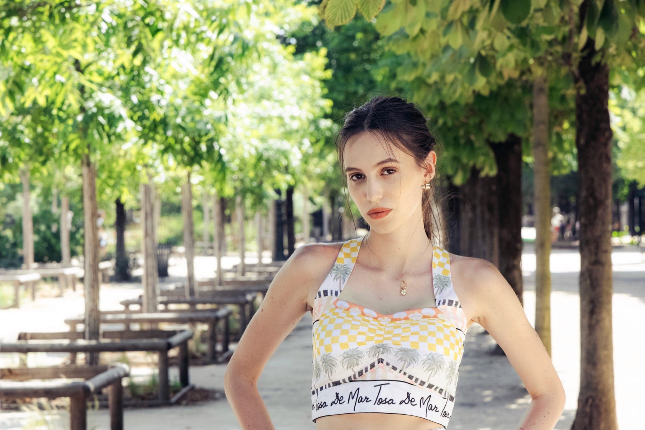 Crop top à damier jaune et blanc, motif de palmiers et inscription « Tosa De Mar », mains sur les hanches.