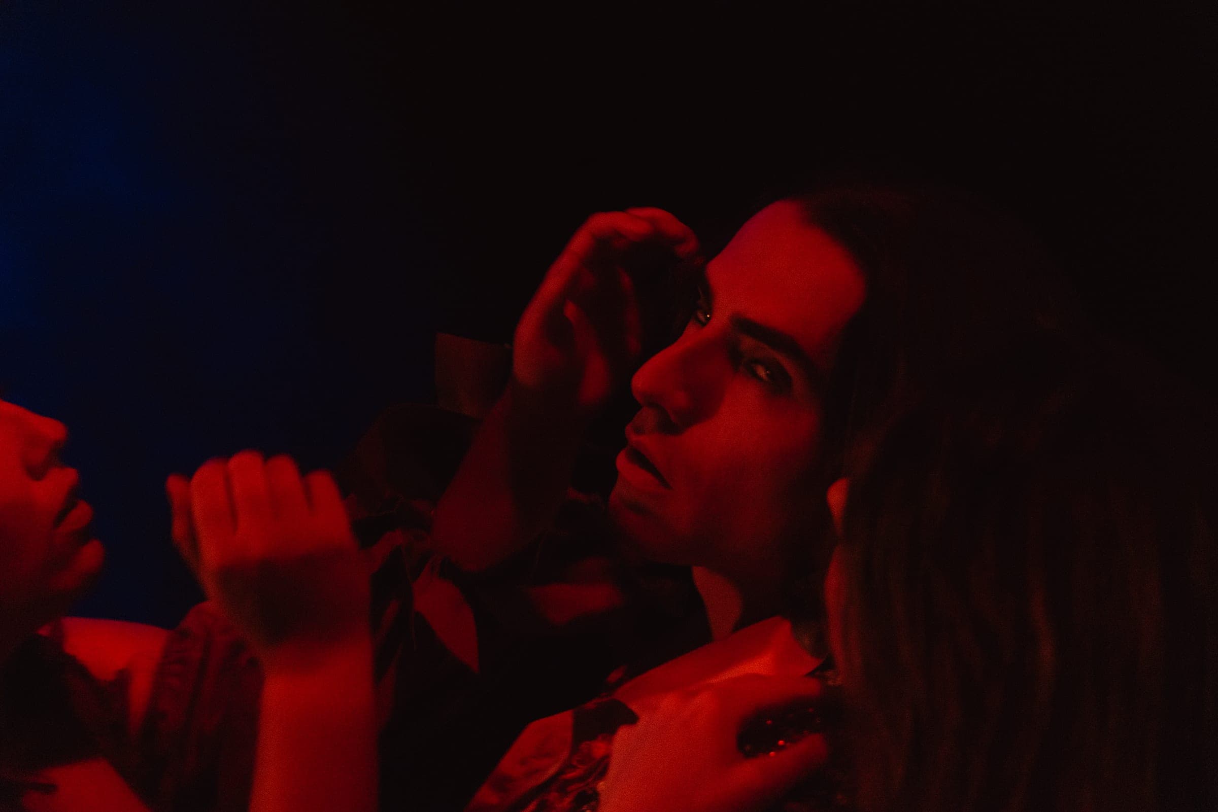 Un comédien renversé au milieu de mains tendues, sous une lumière rouge
