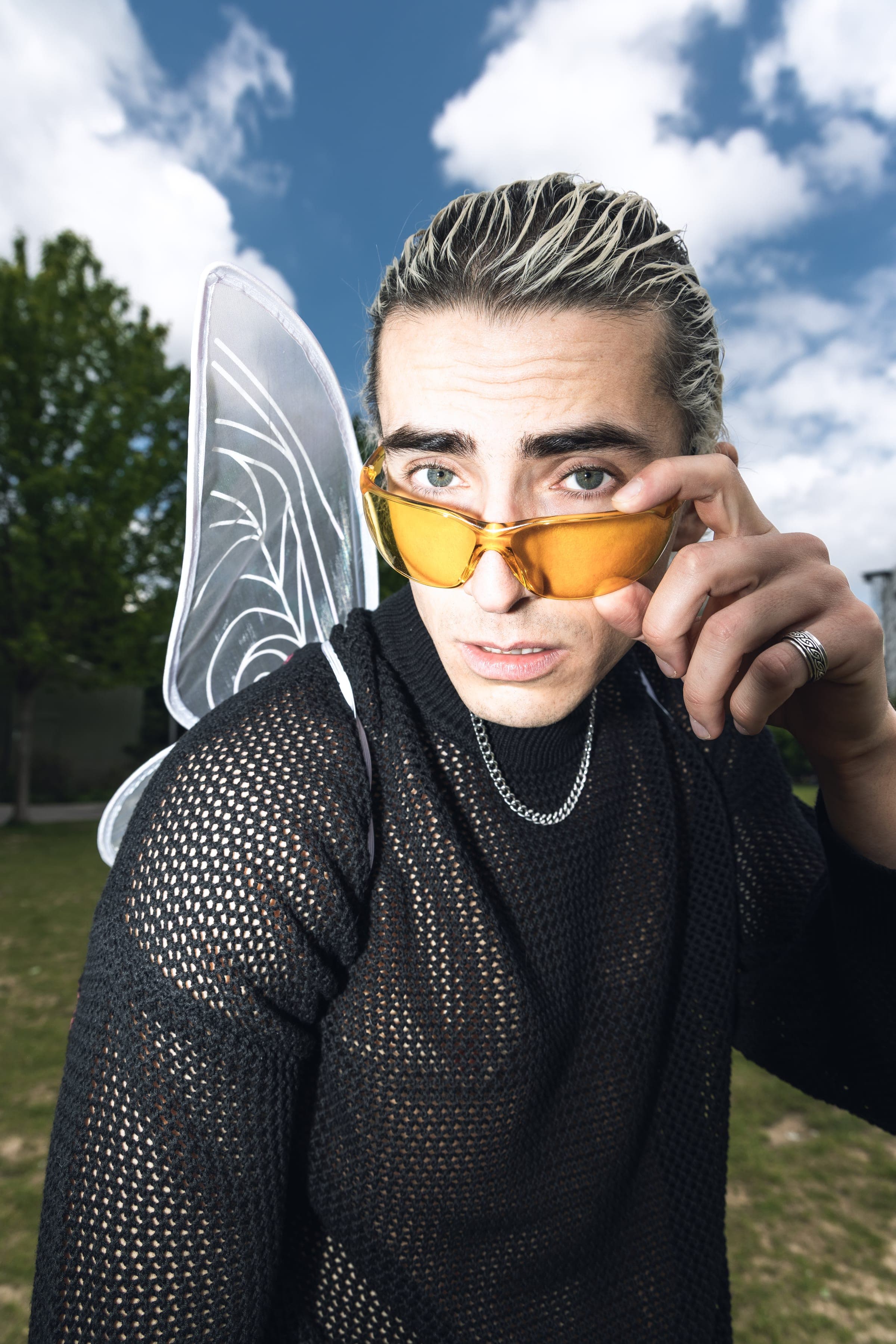 Il abaisse ses lunettes jaunes, ailes déployées, ciel bleu et nuages.