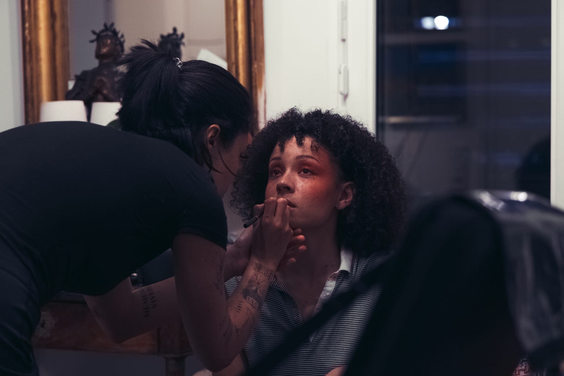 Une maquilleuse termine le maquillage d'une comédienne devant un miroir doré