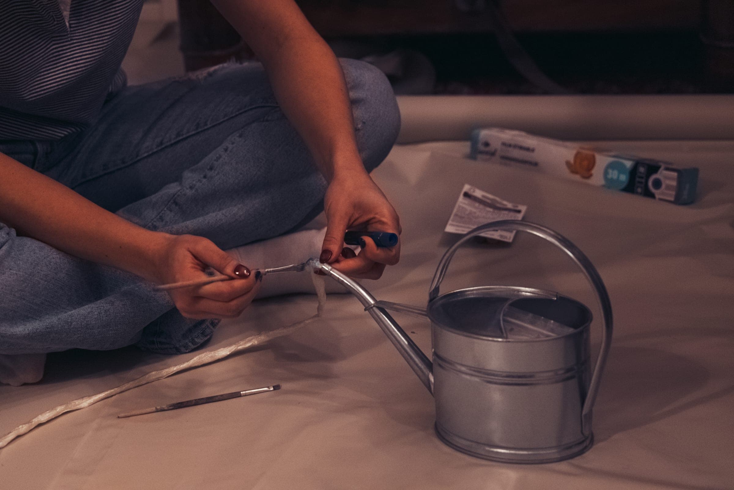 Assis par terre, quelqu'un fixe un embout au bec d'un arrosoir en zinc
