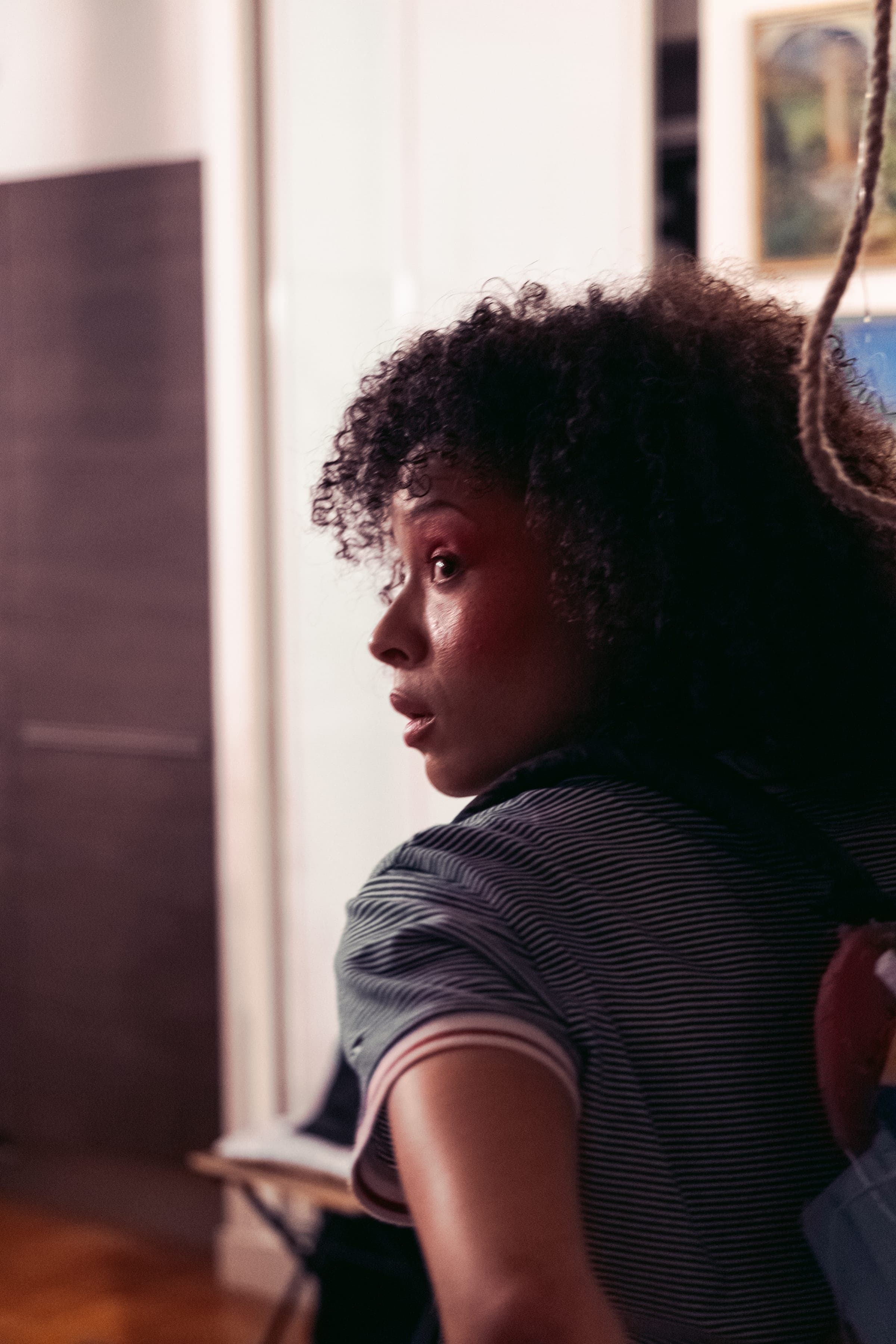 La même comédienne de profil, sac sur l'épaule, dans l'appartement