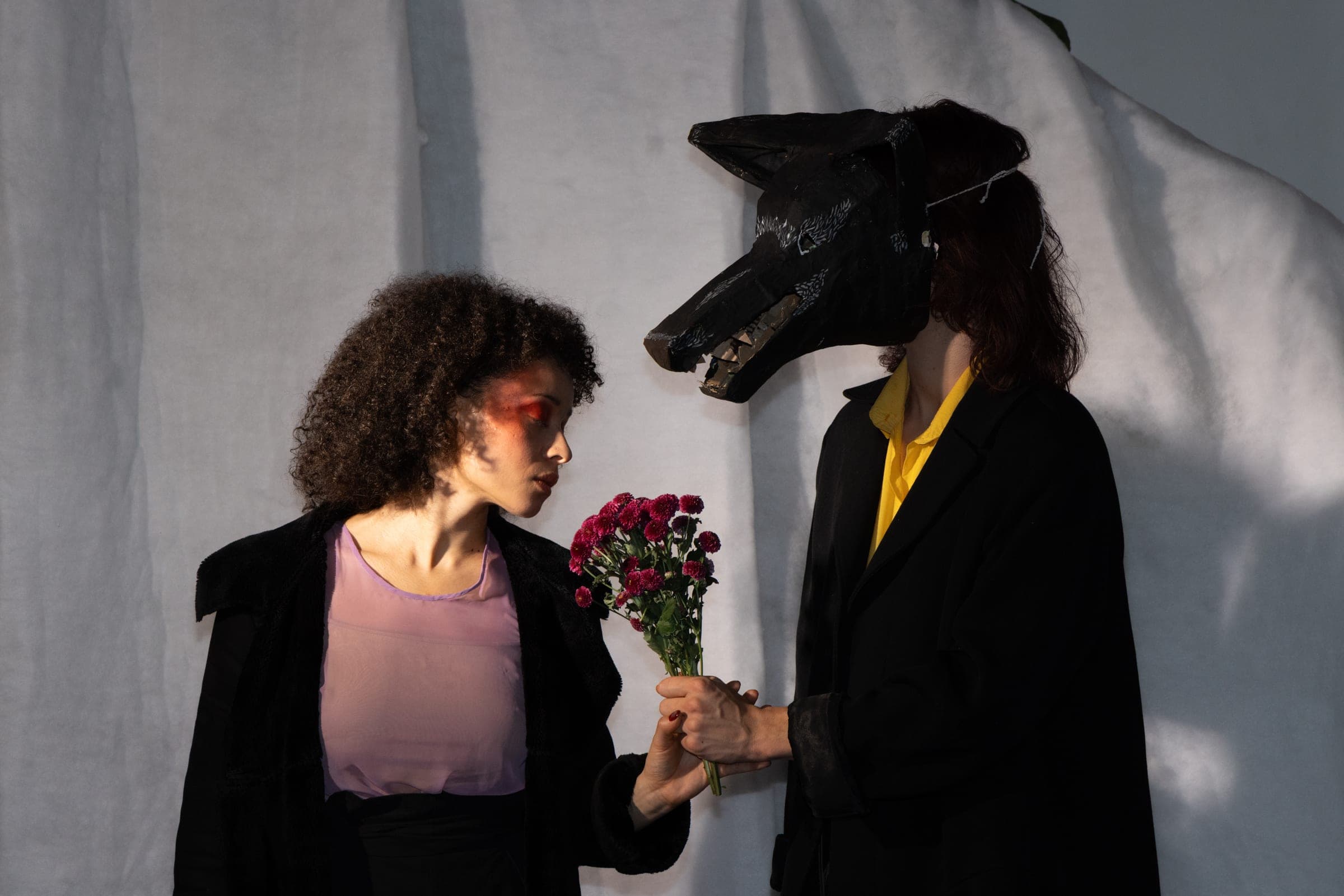 Un personnage masqué en loup tend un bouquet à la comédienne