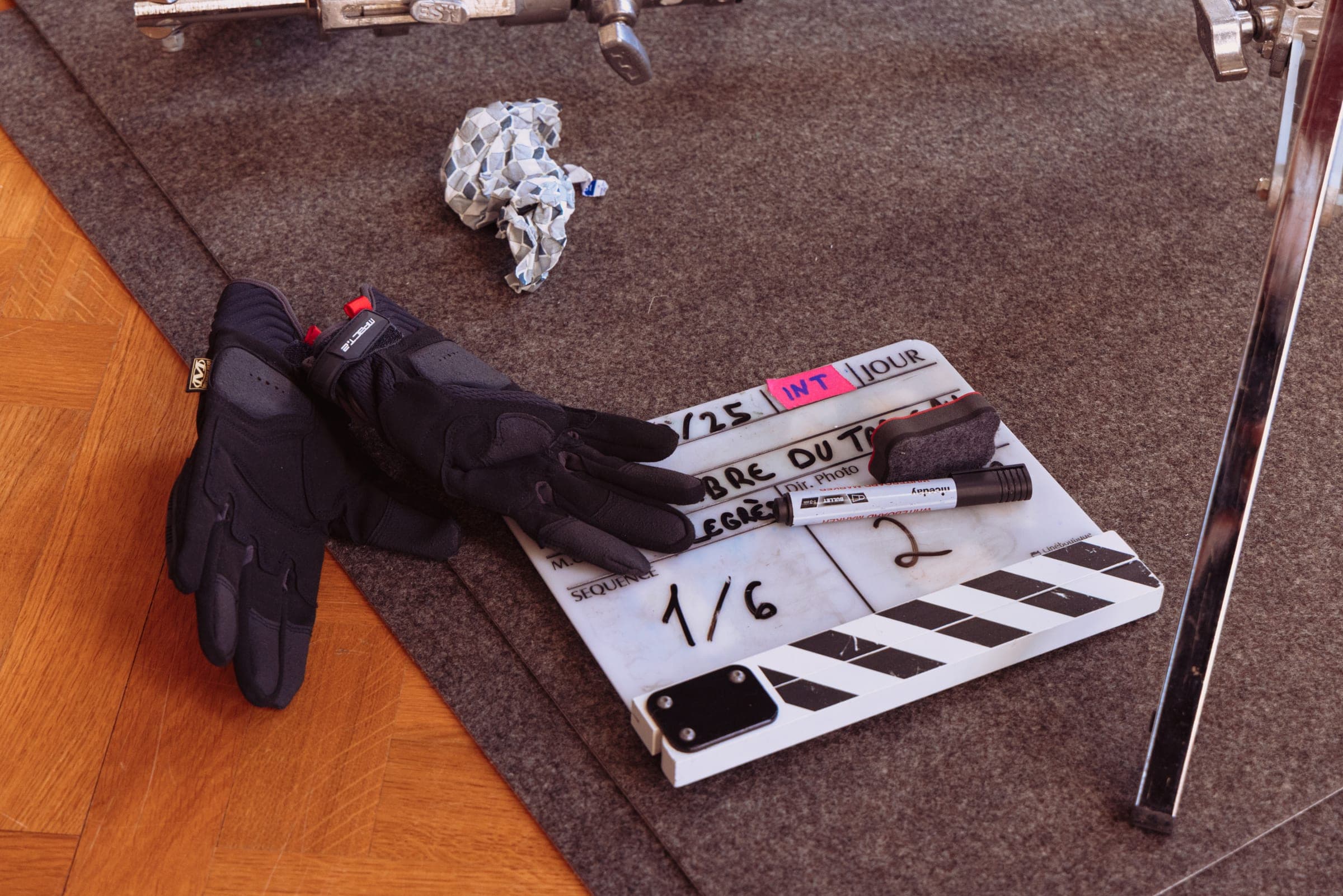 Un clap posé au sol à côté d'une paire de gants noirs, sur la moquette du décor.