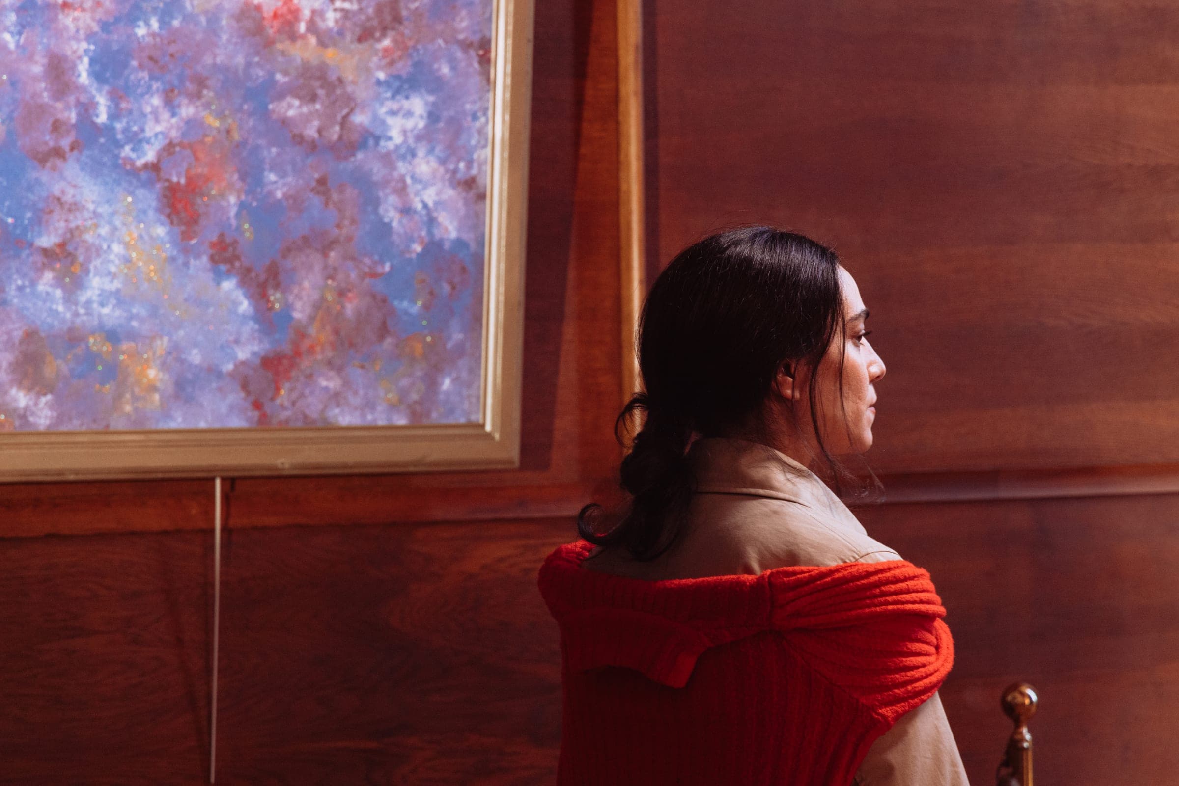 La comédienne à l'écharpe rouge de trois quarts dos, face au tableau.