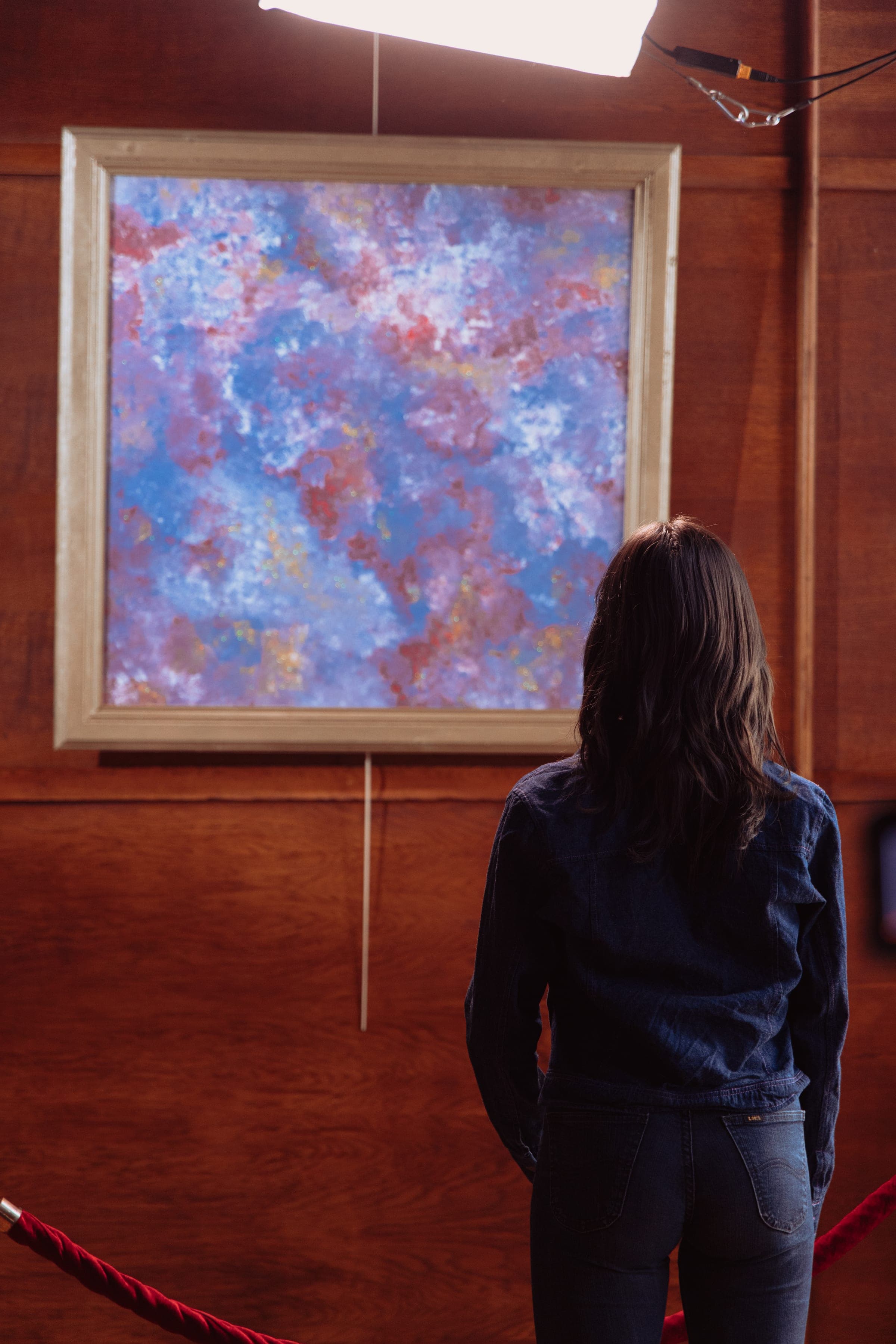 Une comédienne de dos devant la toile, le cordon rouge au premier plan.