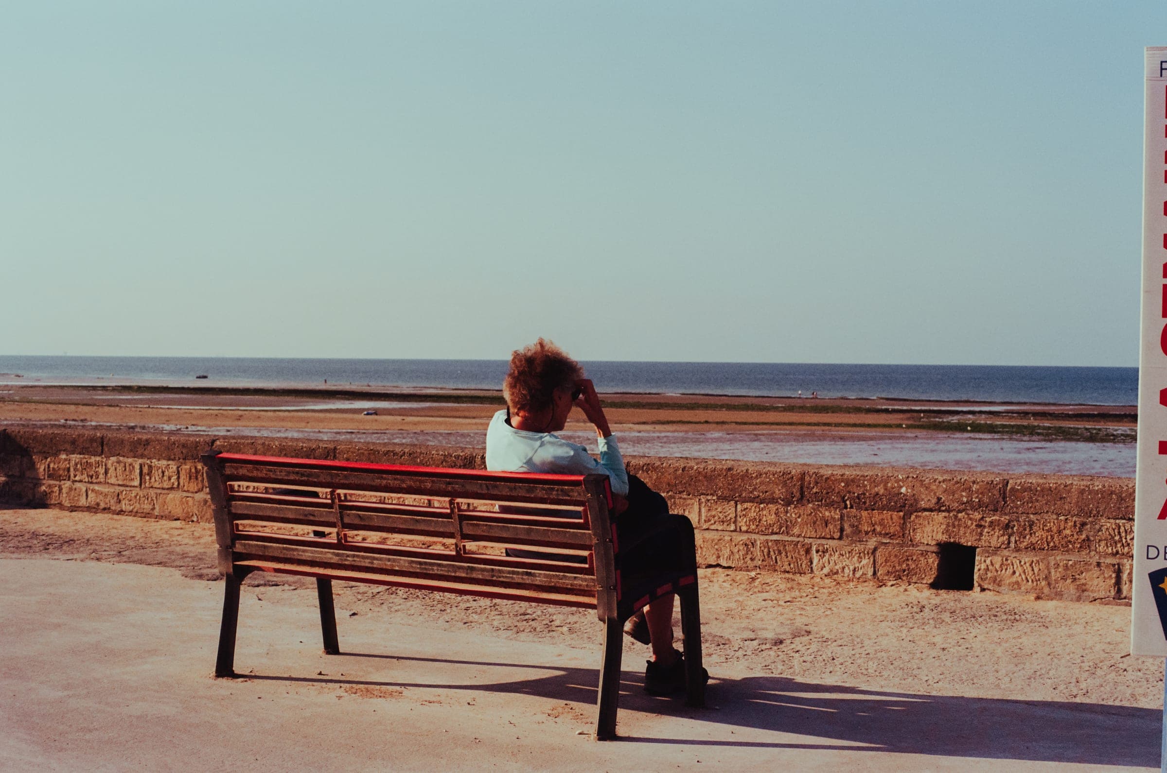 Une femme seule sur un banc, face à la mer, à marée basse.