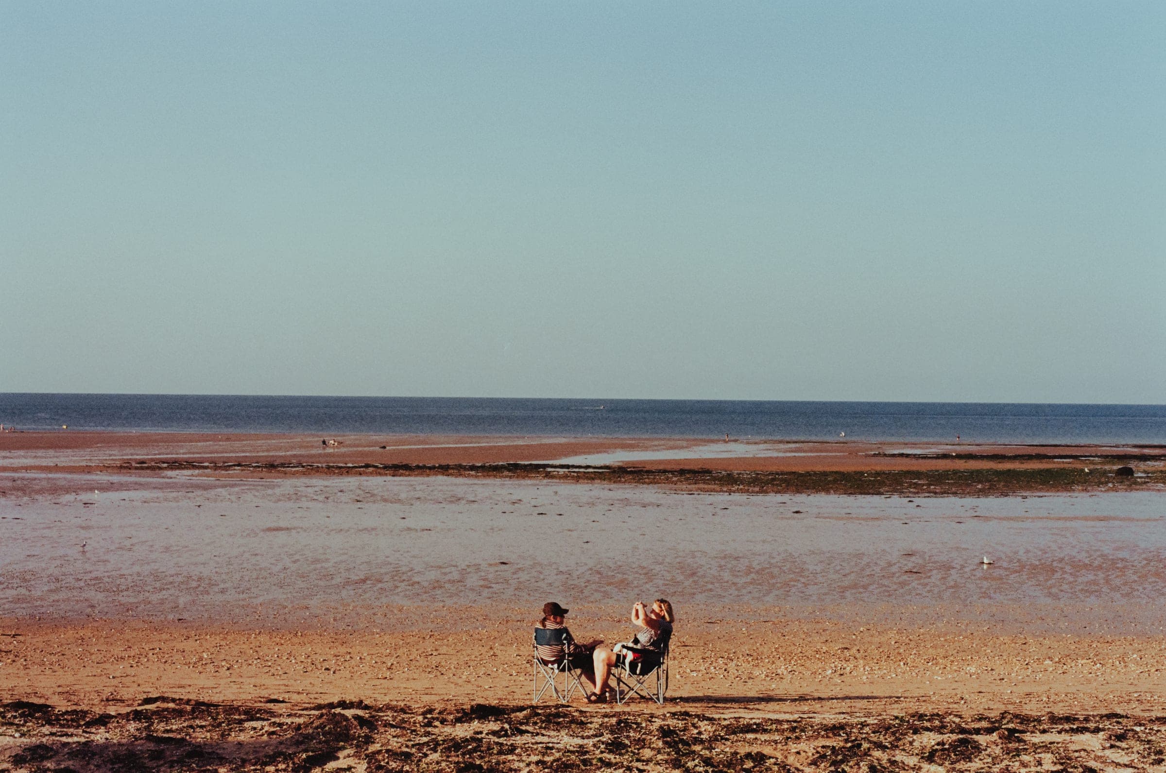 Un couple assis sur le sable mouillé, la marée est loin derrière.