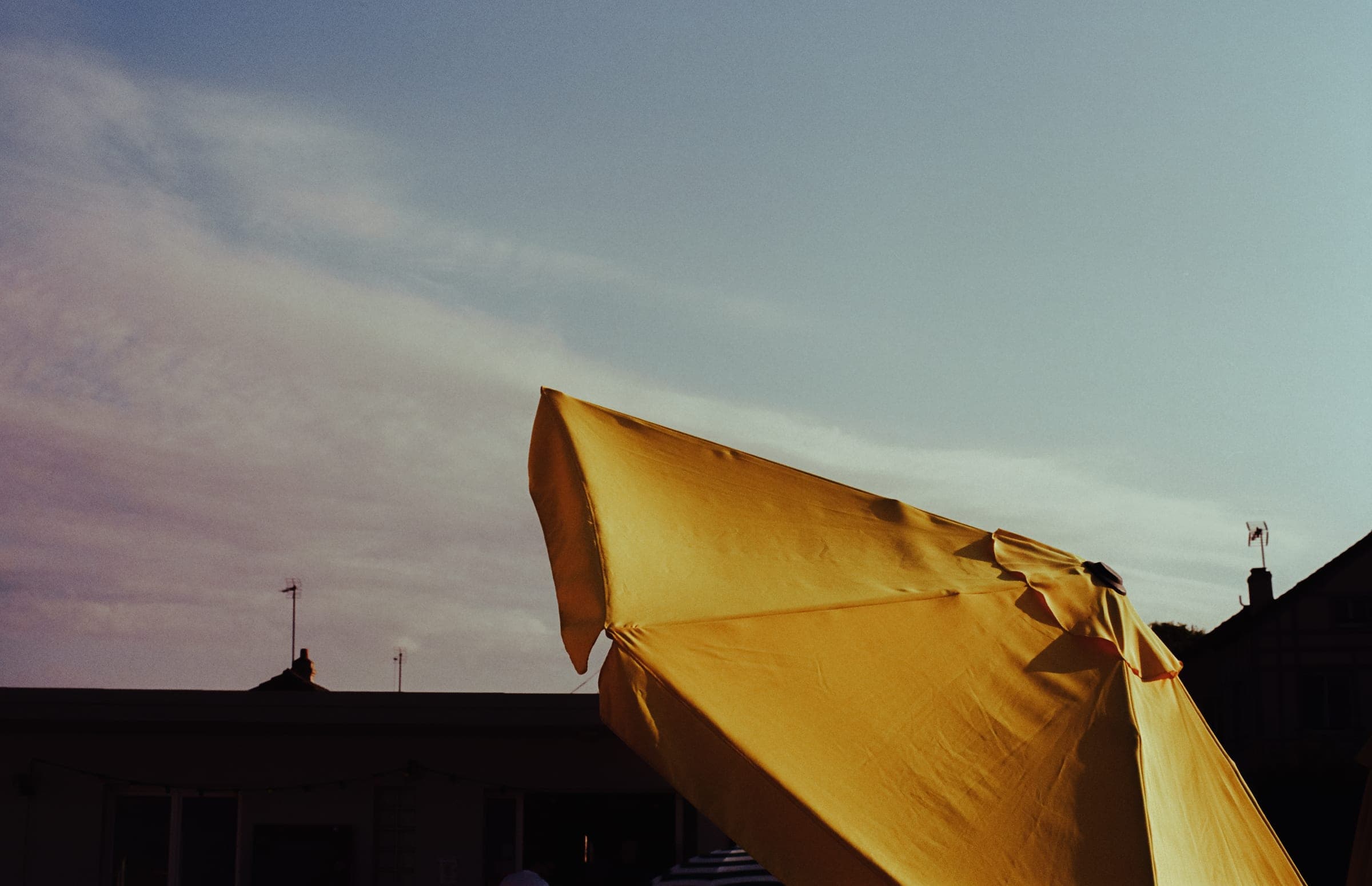Un parasol jaune claque au vent au-dessus d'un toit sombre.