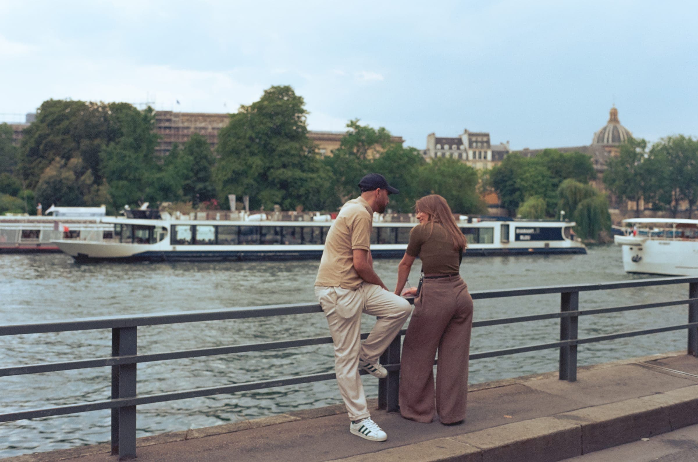 Un couple discute au bord de la Seine, une péniche passe derrière eux.