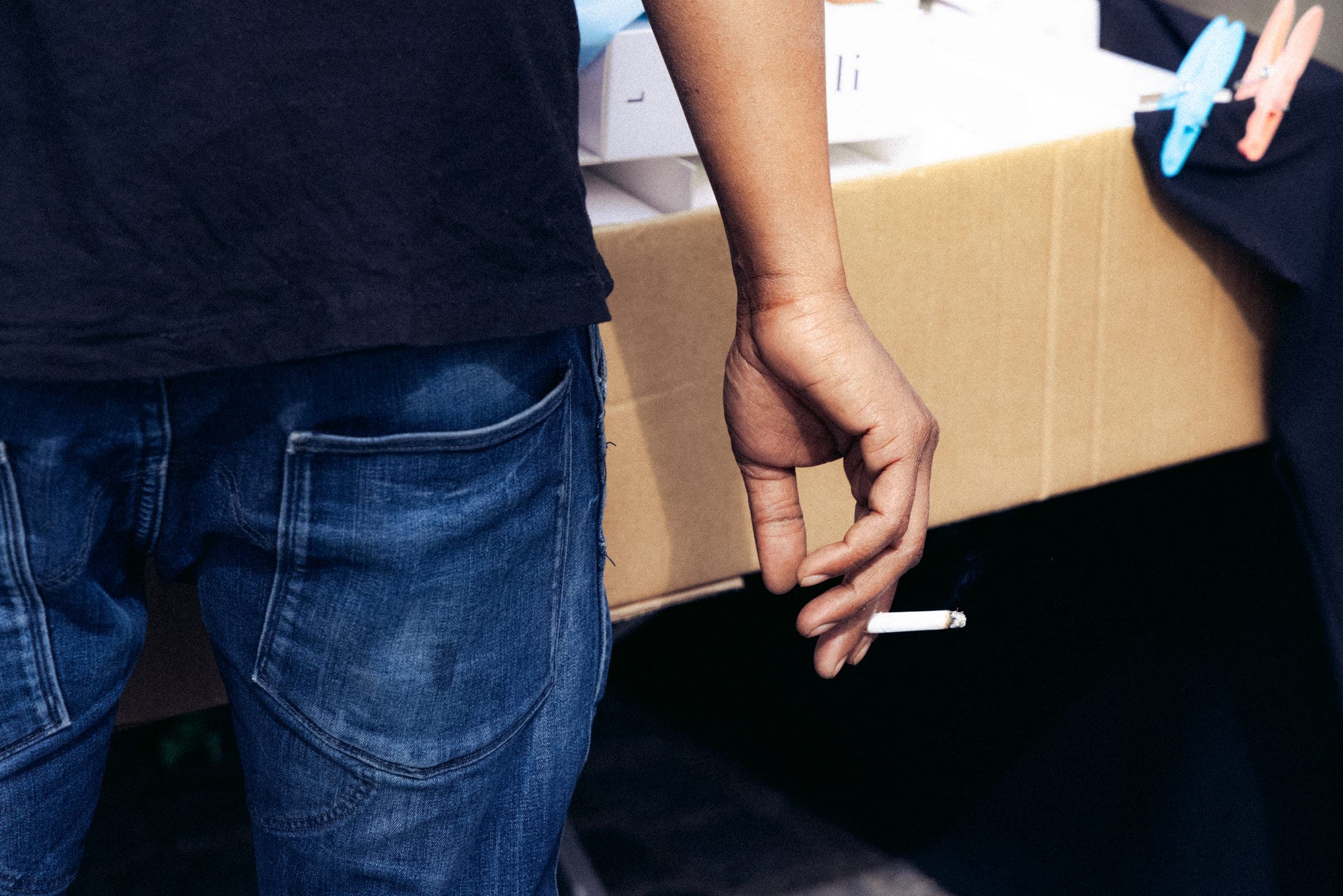 Un homme porte un carton sous le bras, cigarette au bout des doigts.