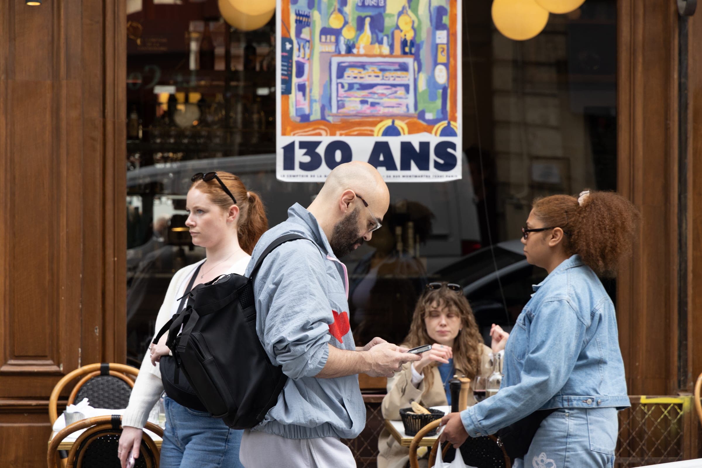 Des passants devant une terrasse et une affiche annonçant 130 ans.