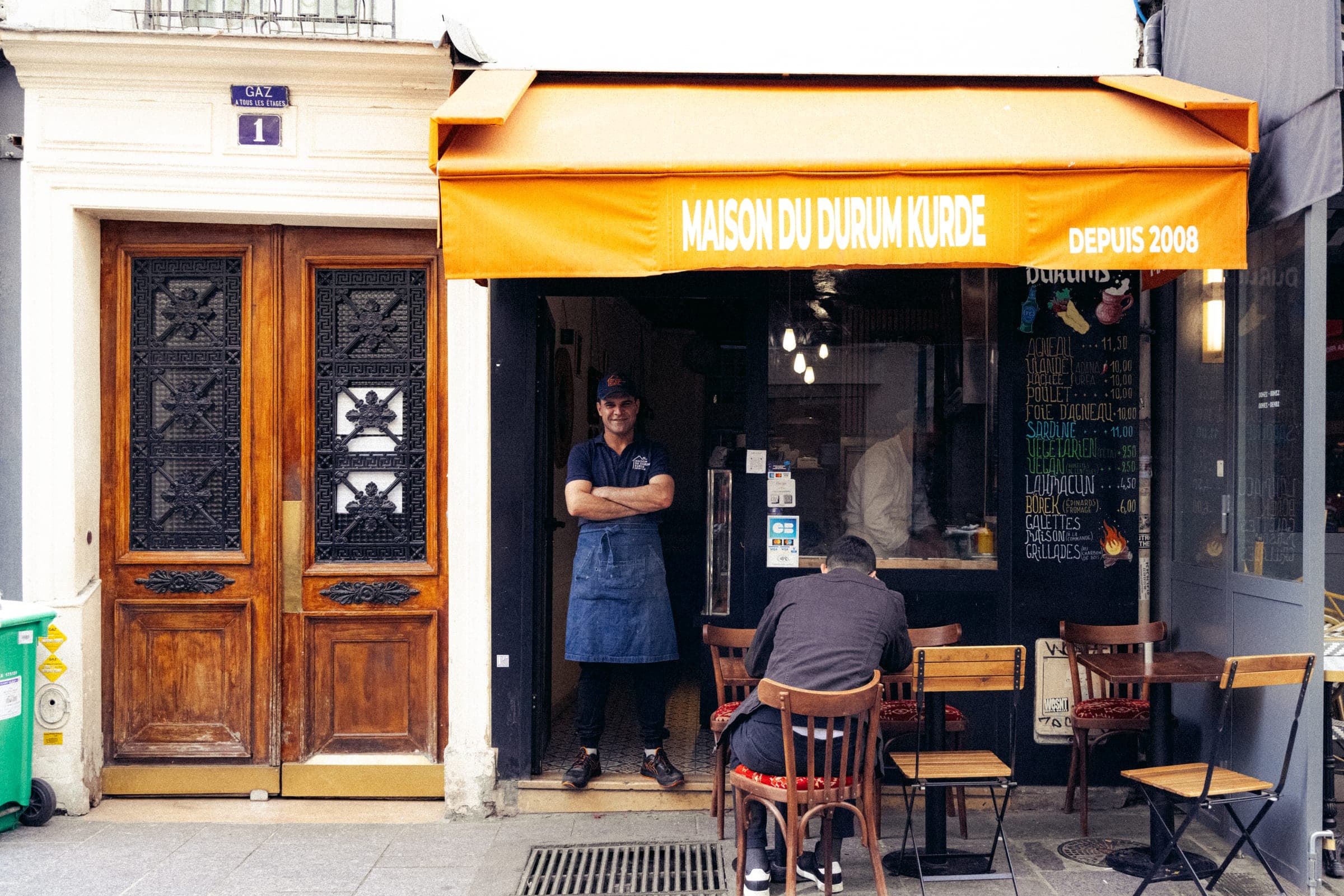 La devanture jaune d'un restaurant kurde, le patron sur le pas de la porte.