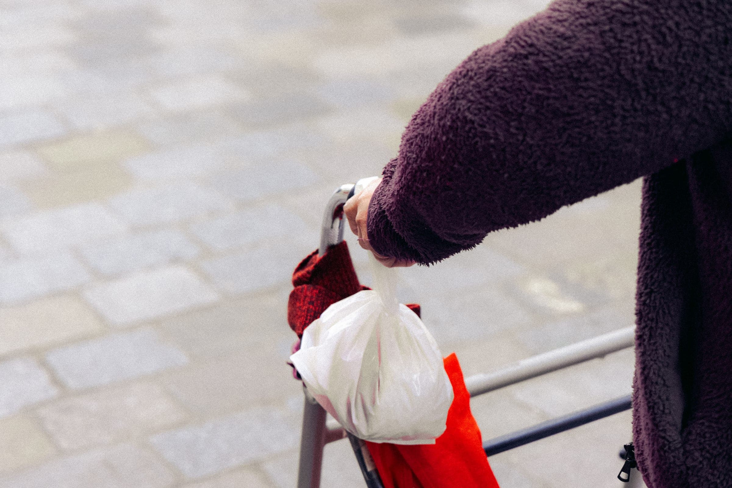 Une main tient un sac plastique par-dessus une rambarde.