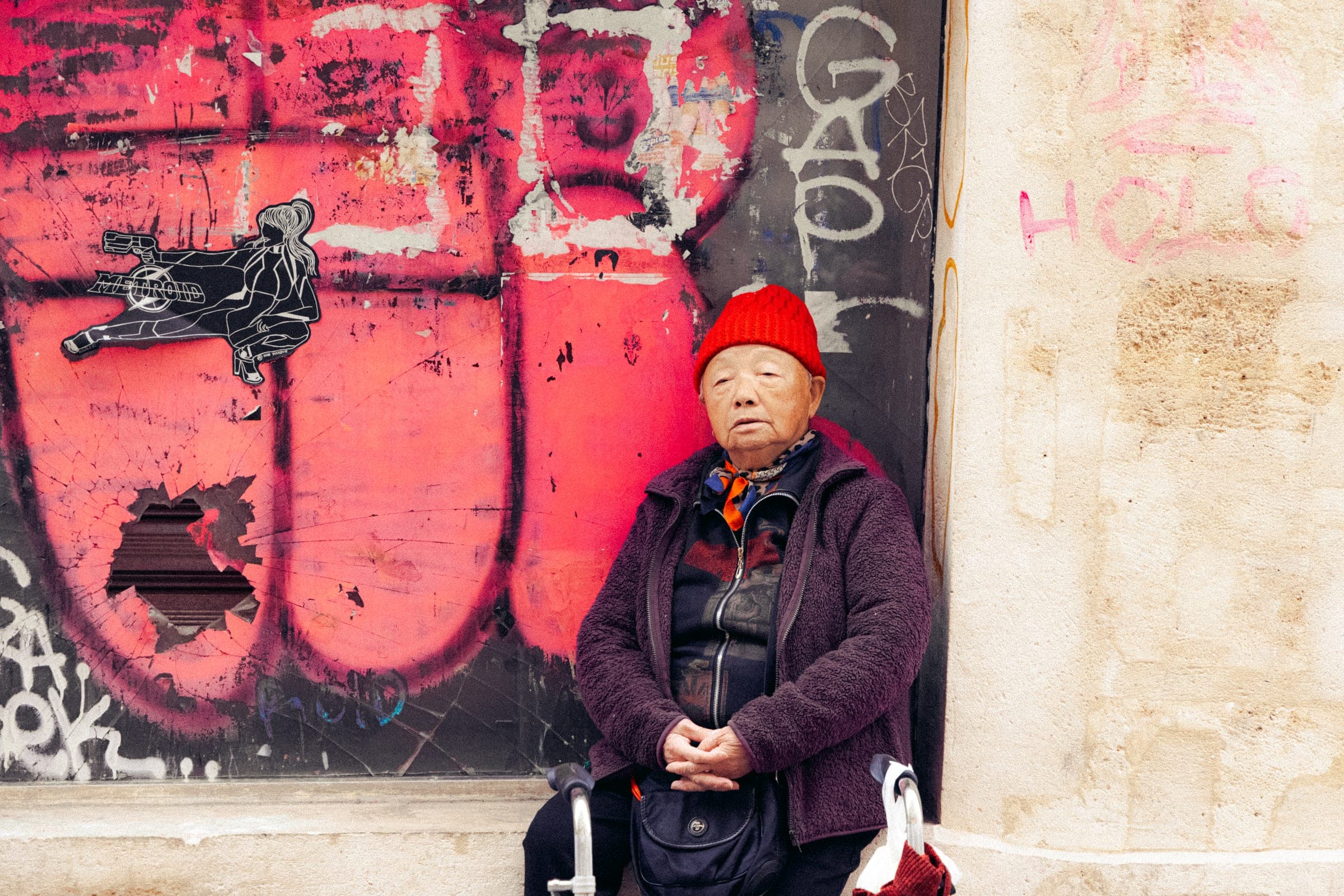Une femme au bonnet rouge assise contre un mur couvert de graffitis.