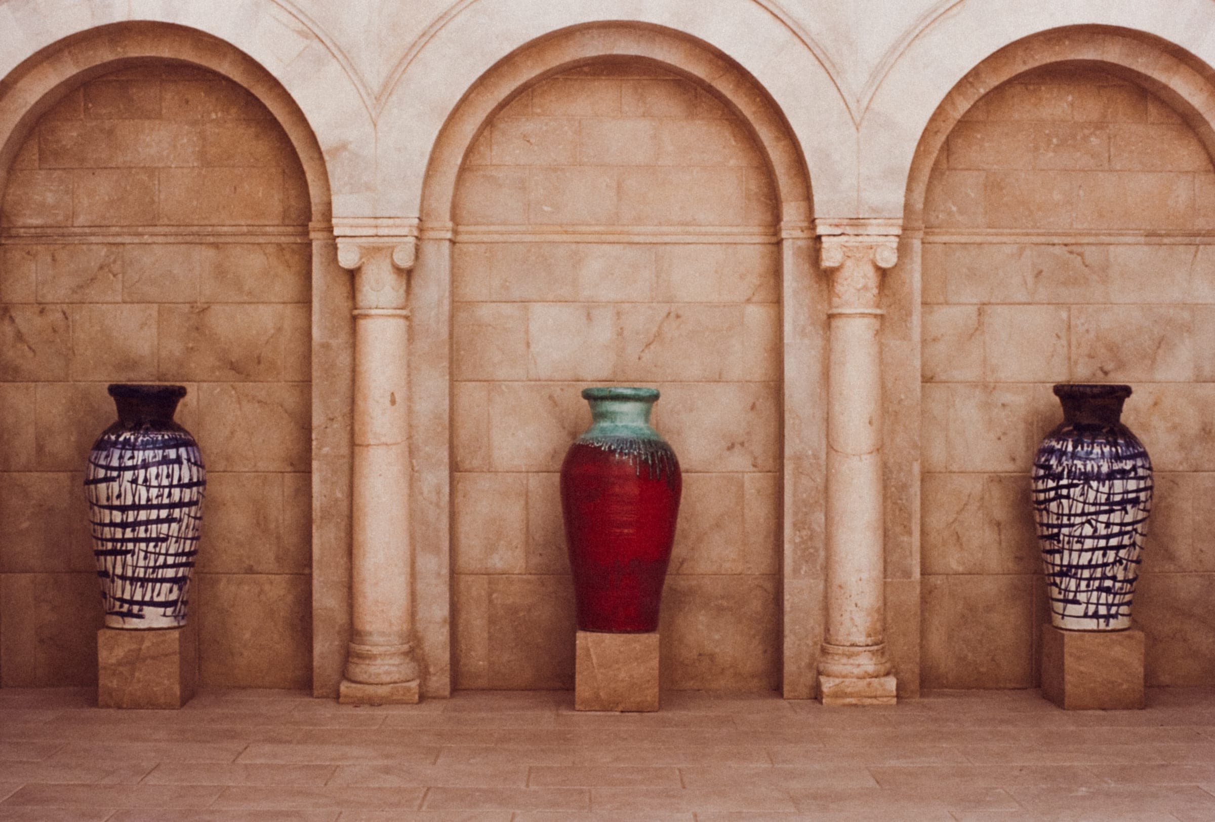Trois jarres posées sous des arcades de pierre claire.