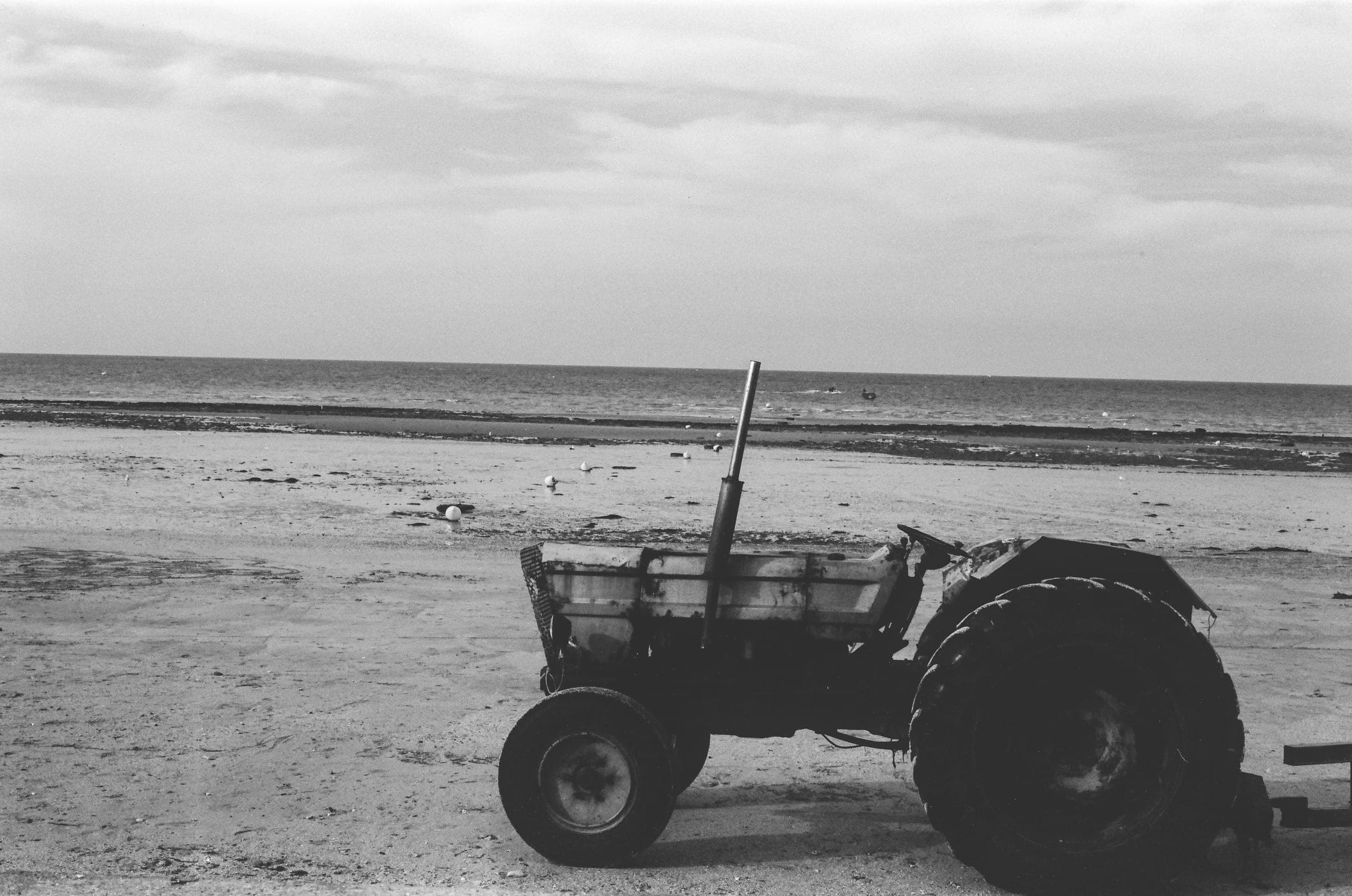 Un vieux tracteur garé sur la plage, mer basse et mouettes derrière.