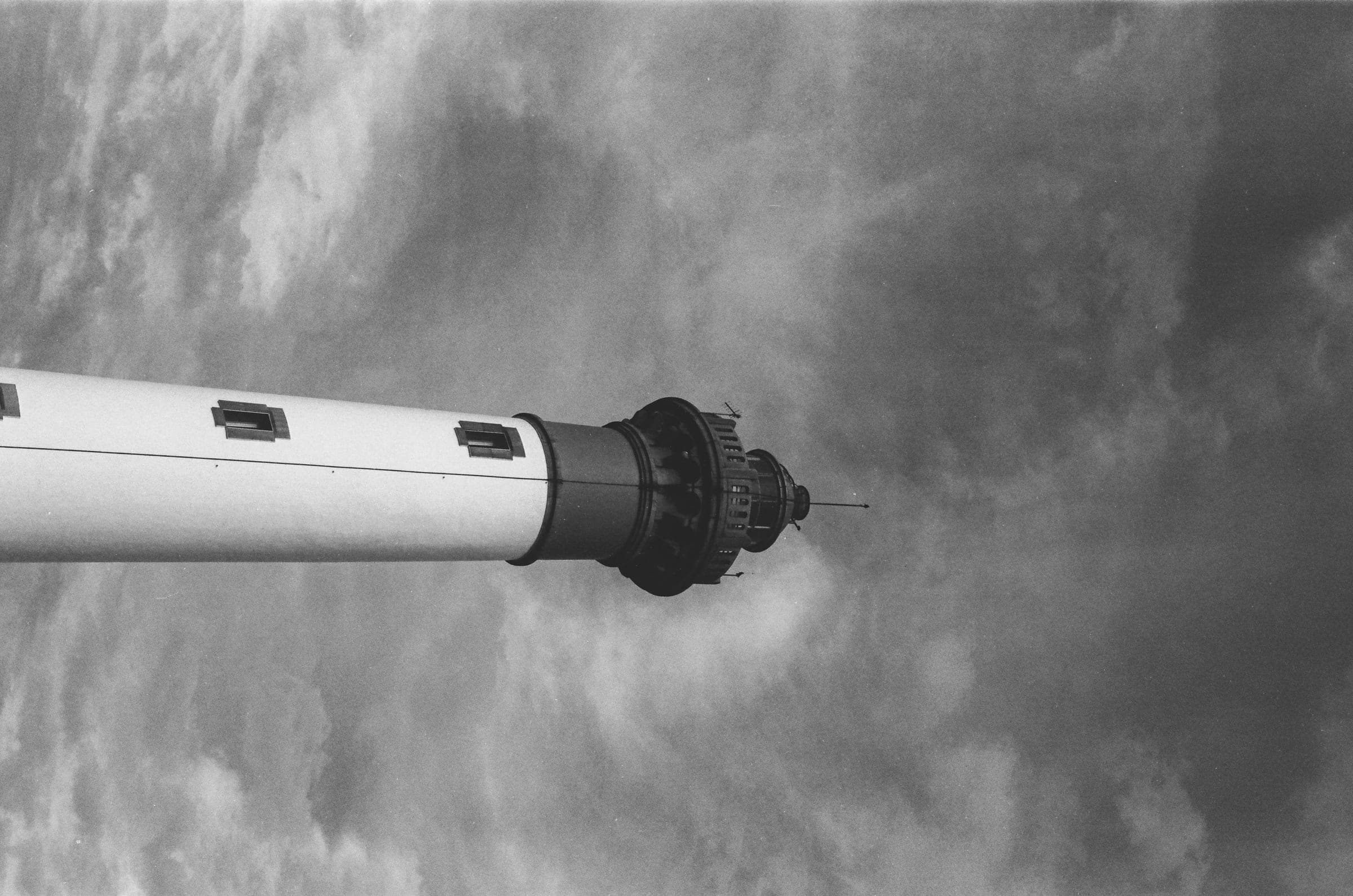 Le sommet d'un phare en contre-plongée, lanterne sombre sur un ciel nuageux.