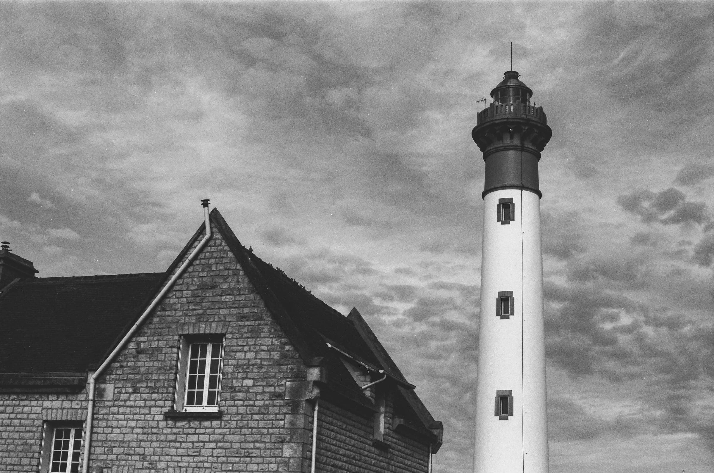 Un phare blanc à lanterne sombre à côté d'une maison en pierre au toit pointu.