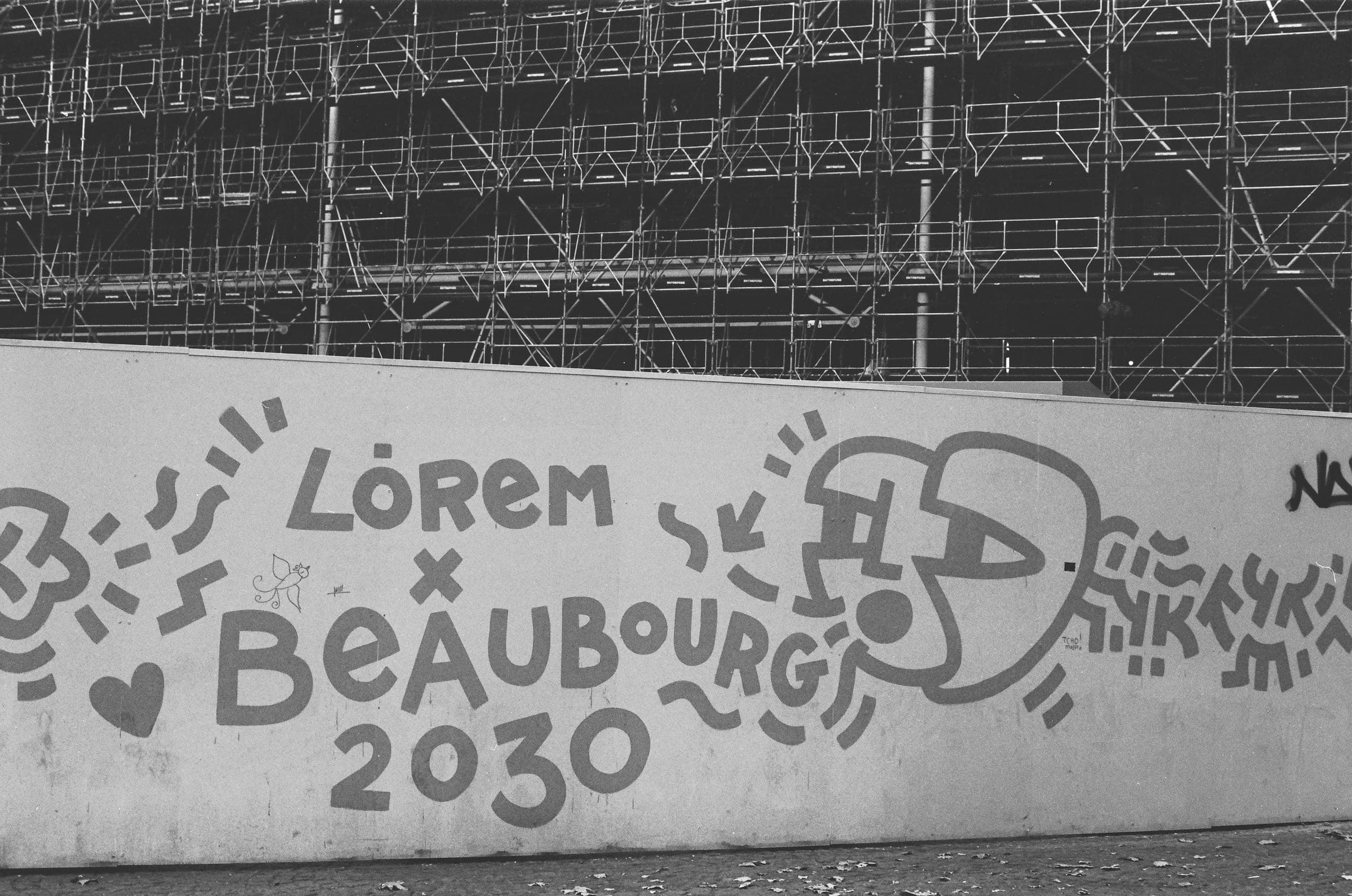 Une palissade de chantier peinte Lorem x Beaubourg 2030, les échafaudages du Centre Pompidou derrière.