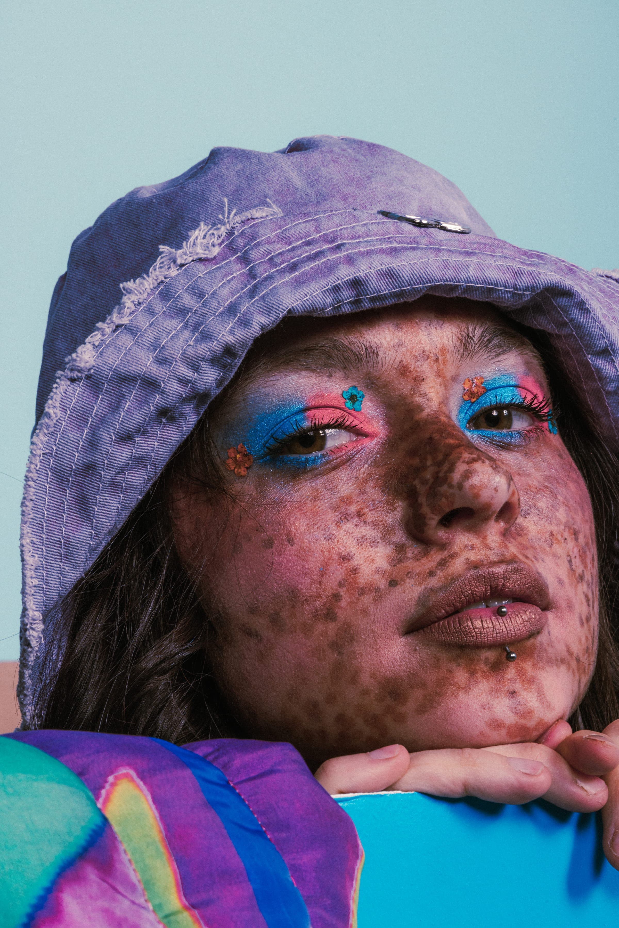 Menton posé sur les mains au bord de la boîte bleue, bob lilas délavé, taches de rousseur et petites fleurs collées sur le fard bleu et rose.
