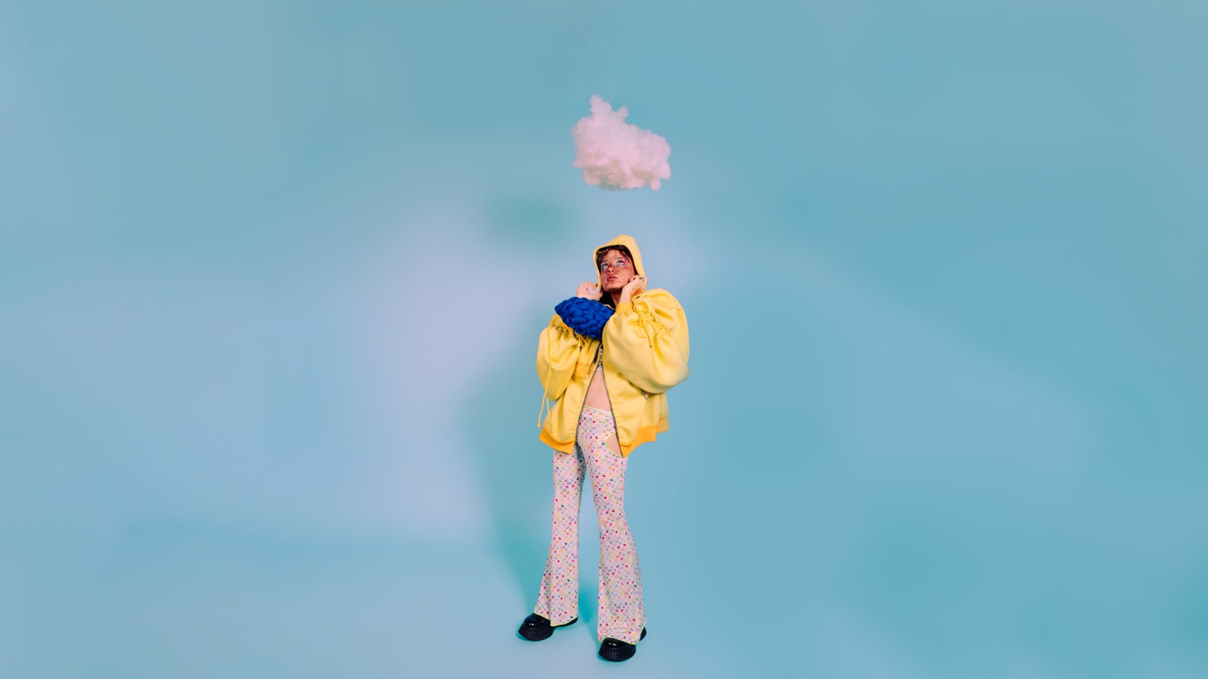 Toute petite au milieu d'un grand fond bleu, capuche jaune sur la tête, un nuage suspendu juste au-dessus.