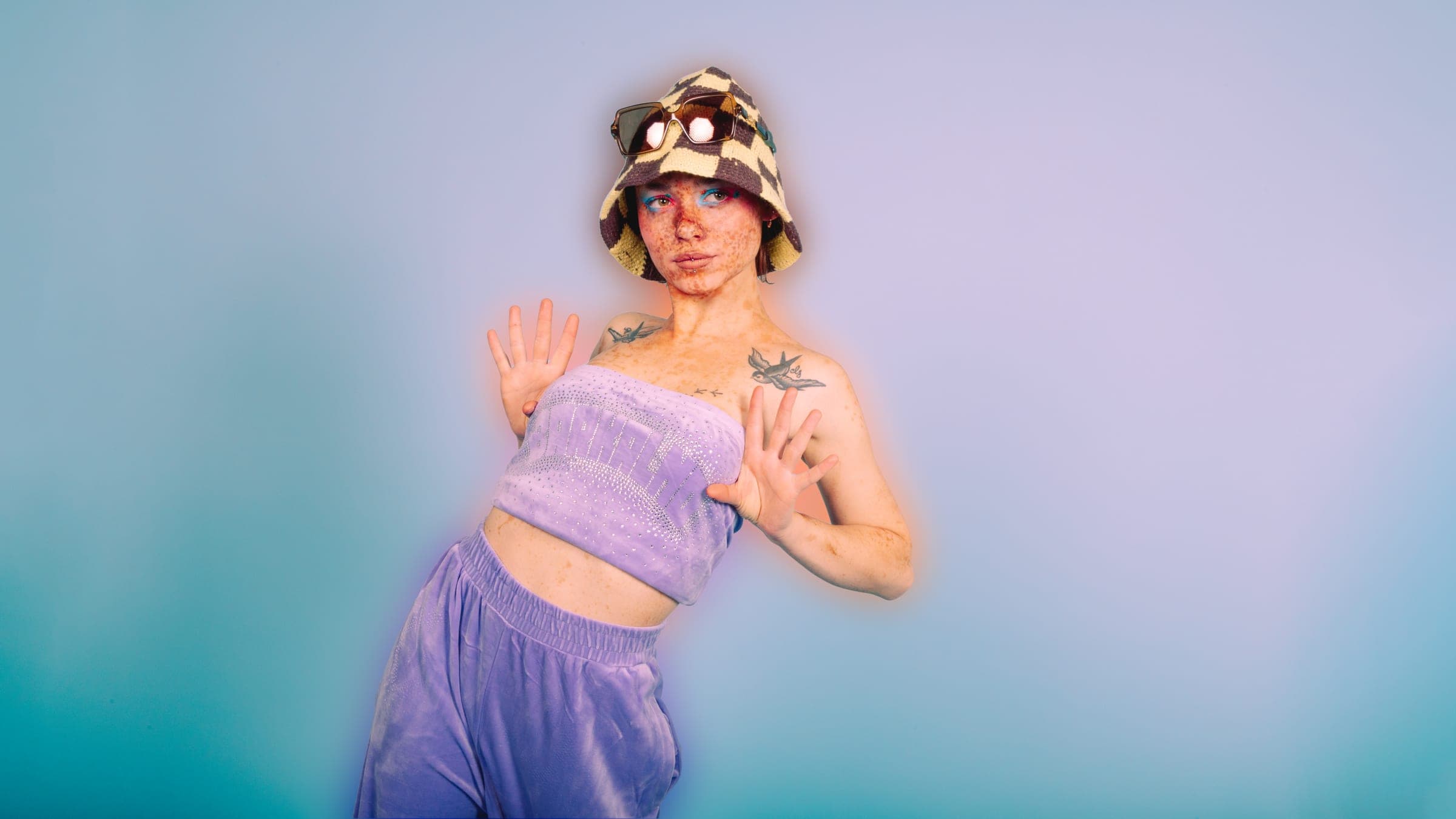 Paumes tendues comme contre une vitre, bob crocheté à damier, bandeau de velours lilas à strass, hirondelles tatouées sur la poitrine.