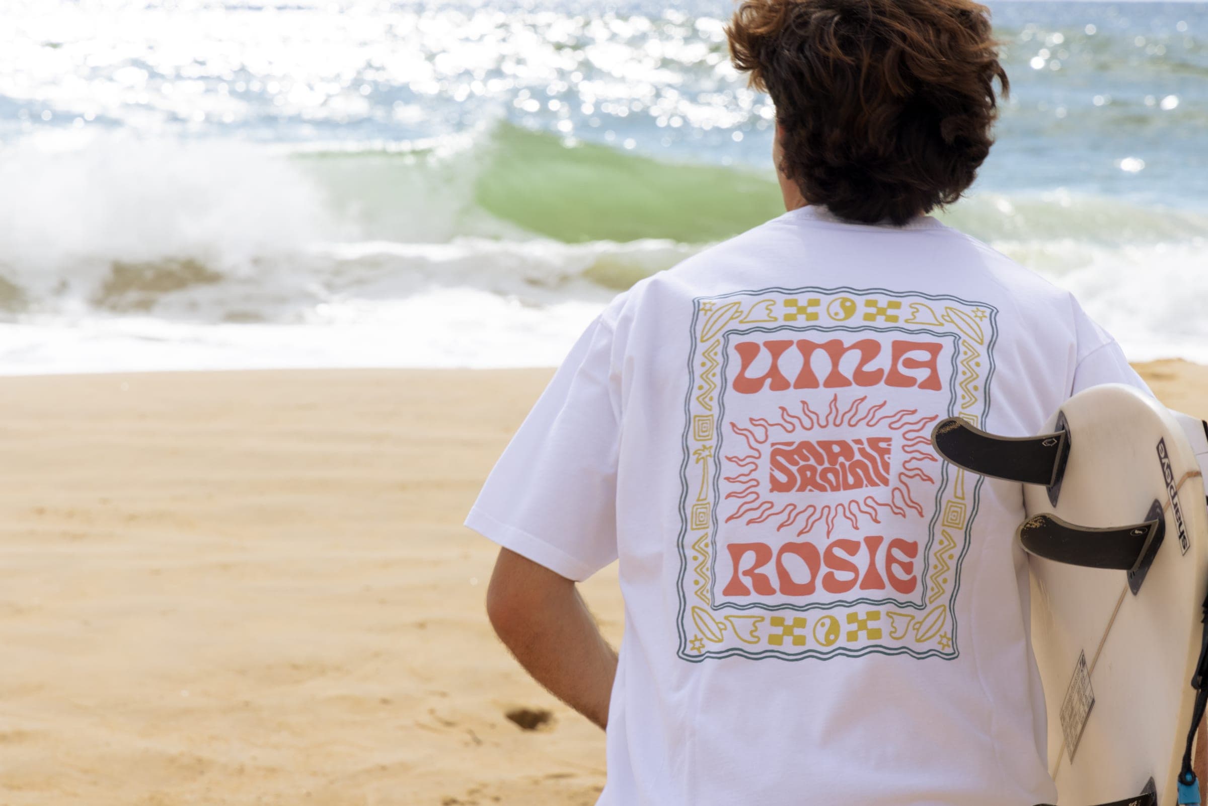 Dos du t-shirt blanc et sa sérigraphie Uma Rosie, face aux vagues.