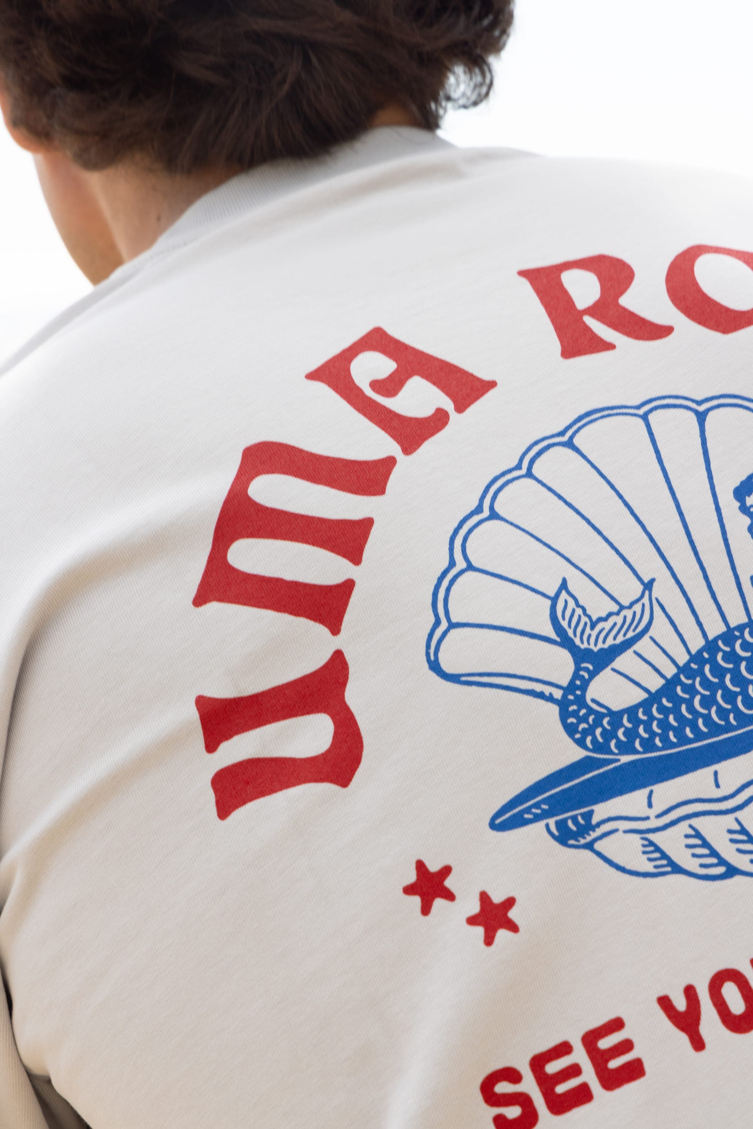 Détail de la sérigraphie : un coquillage bleu et un lettrage rouge sur t-shirt écru.