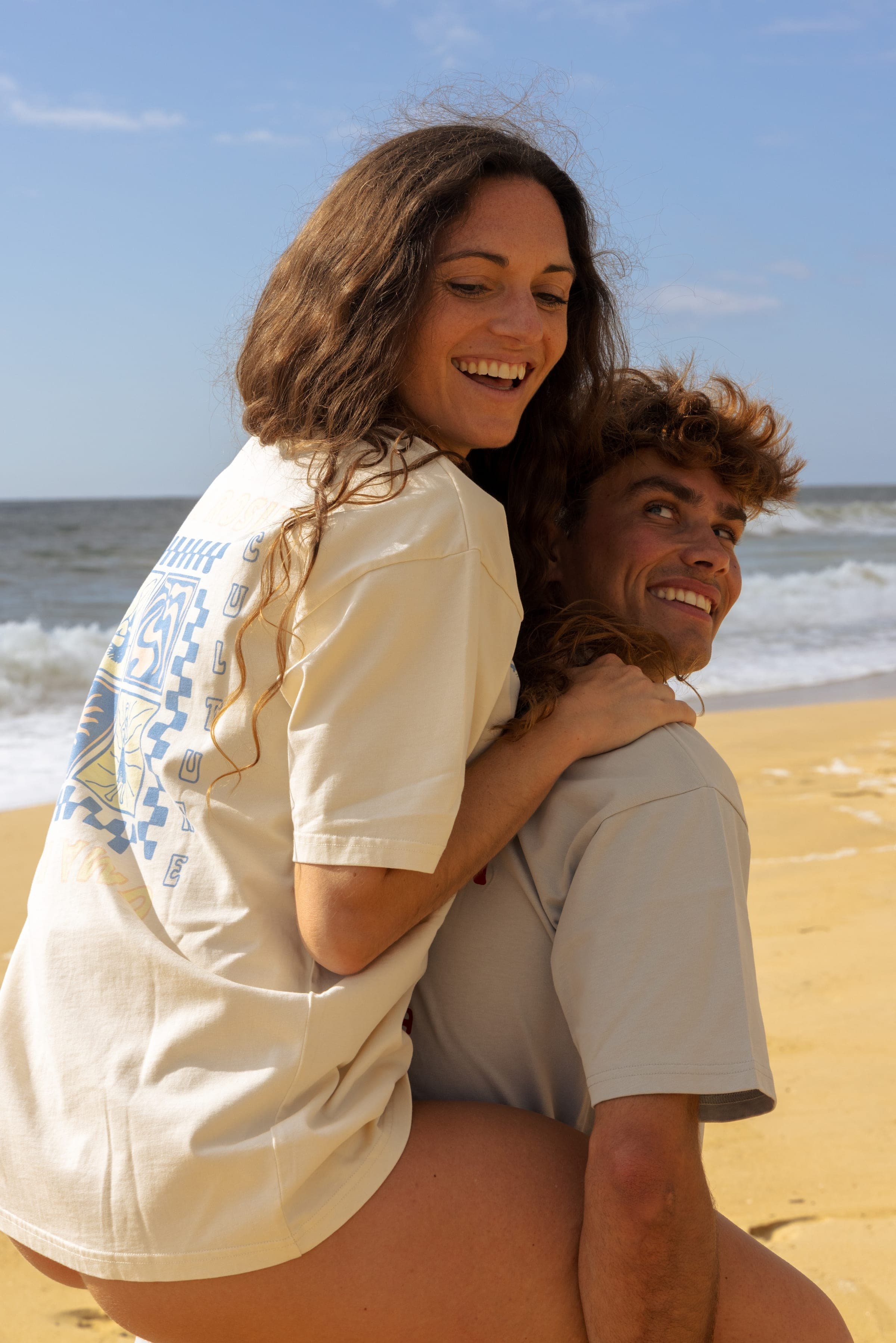 Un couple enlacé sur le sable, le t-shirt écru sérigraphié de dos.