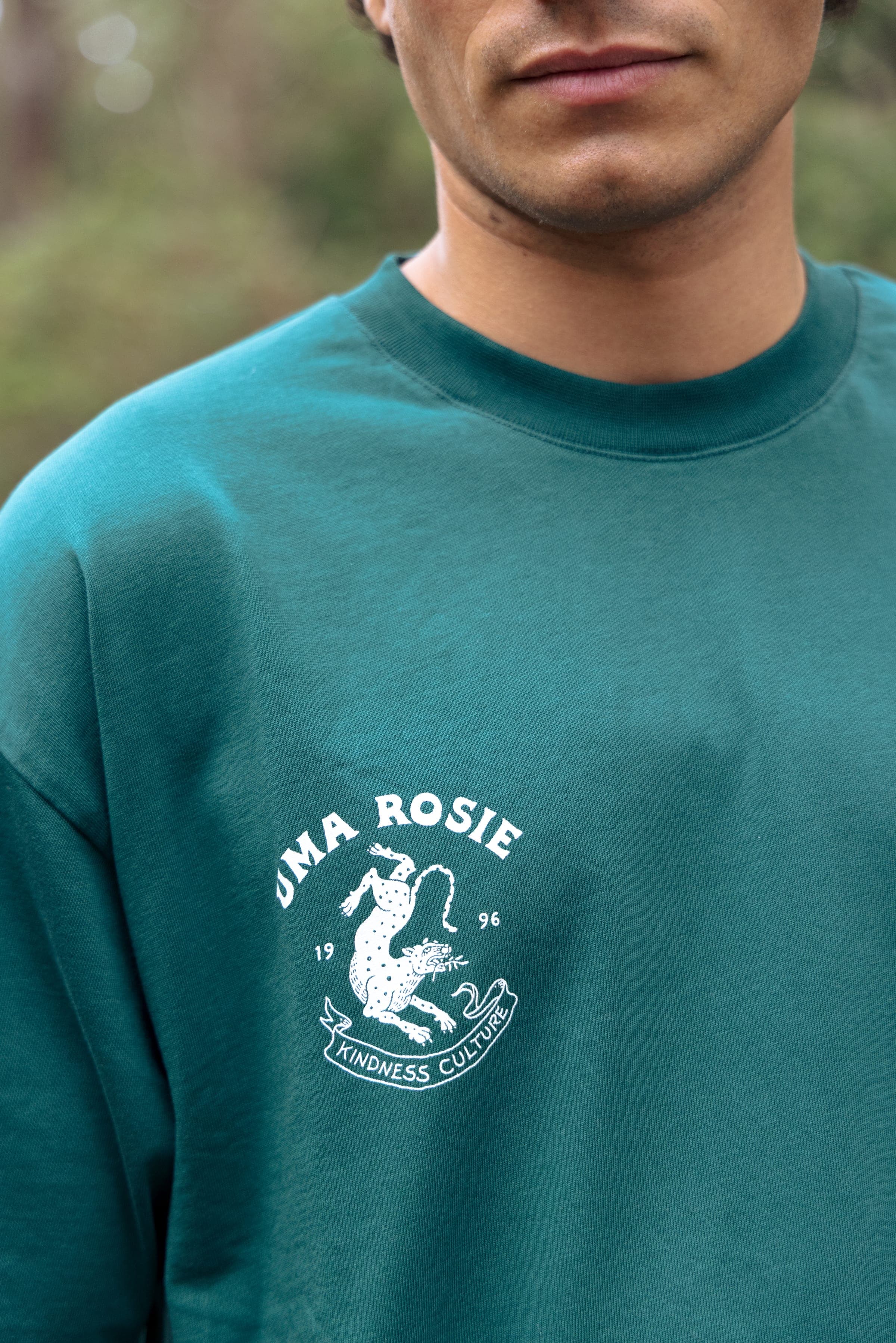 Détail du logo brodé blanc sur le t-shirt vert.