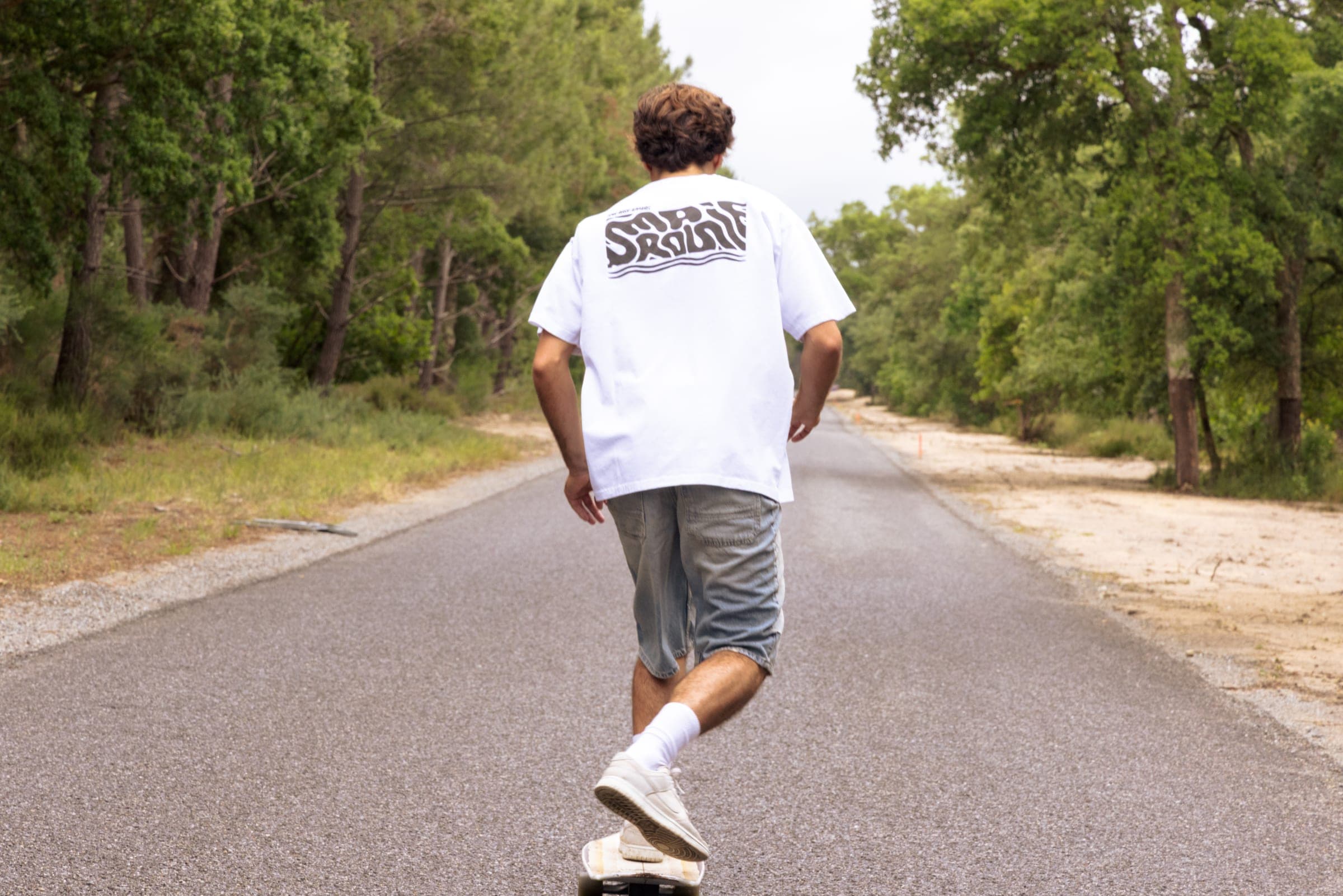 De dos, un skateur remonte la route bordée de pins.