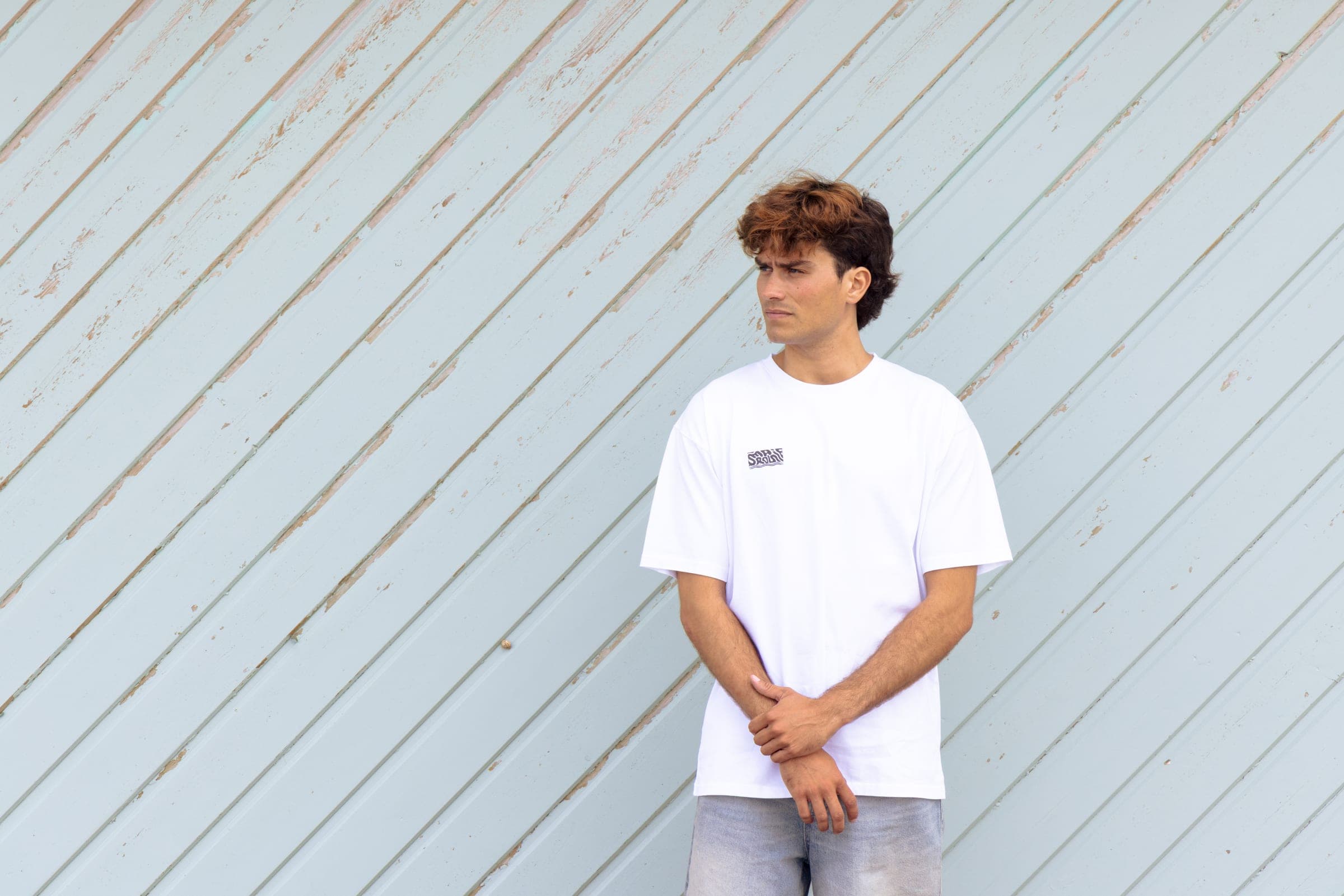 Un homme en t-shirt blanc adossé à un mur de bois clair.