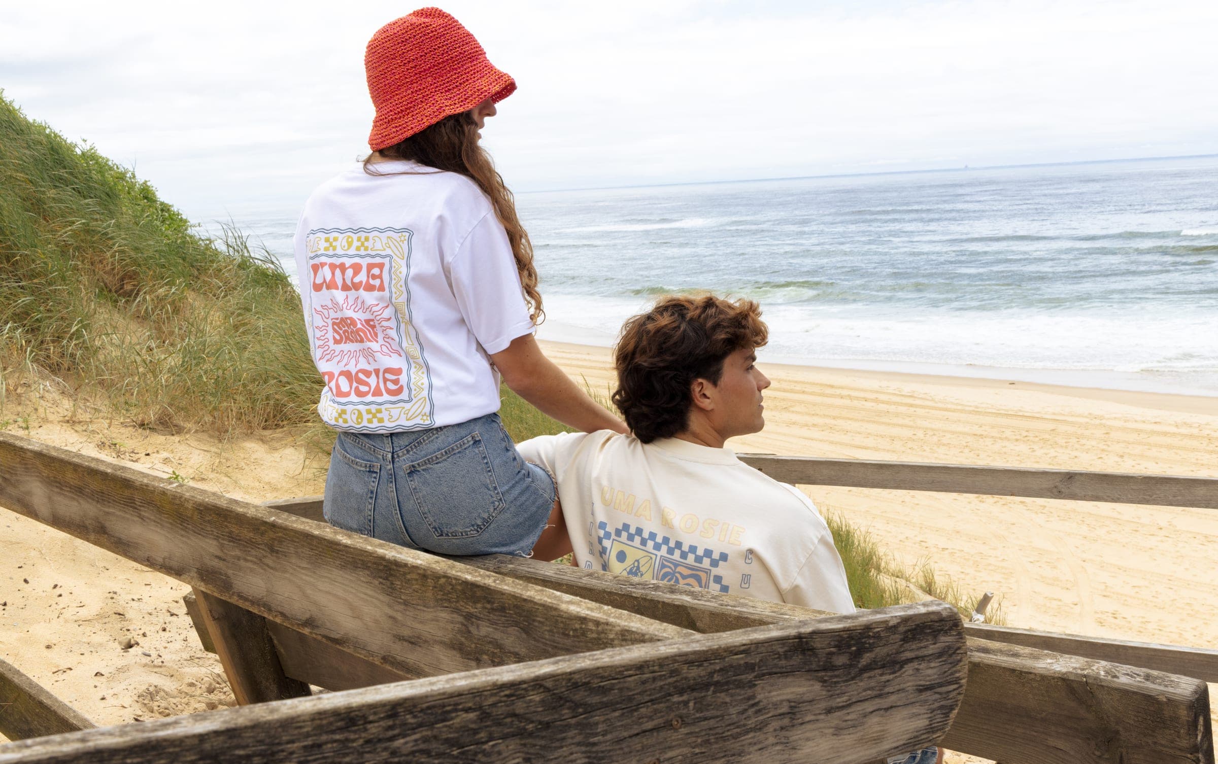 Le couple dans les dunes, elle debout, lui assis sur la rambarde en bois.