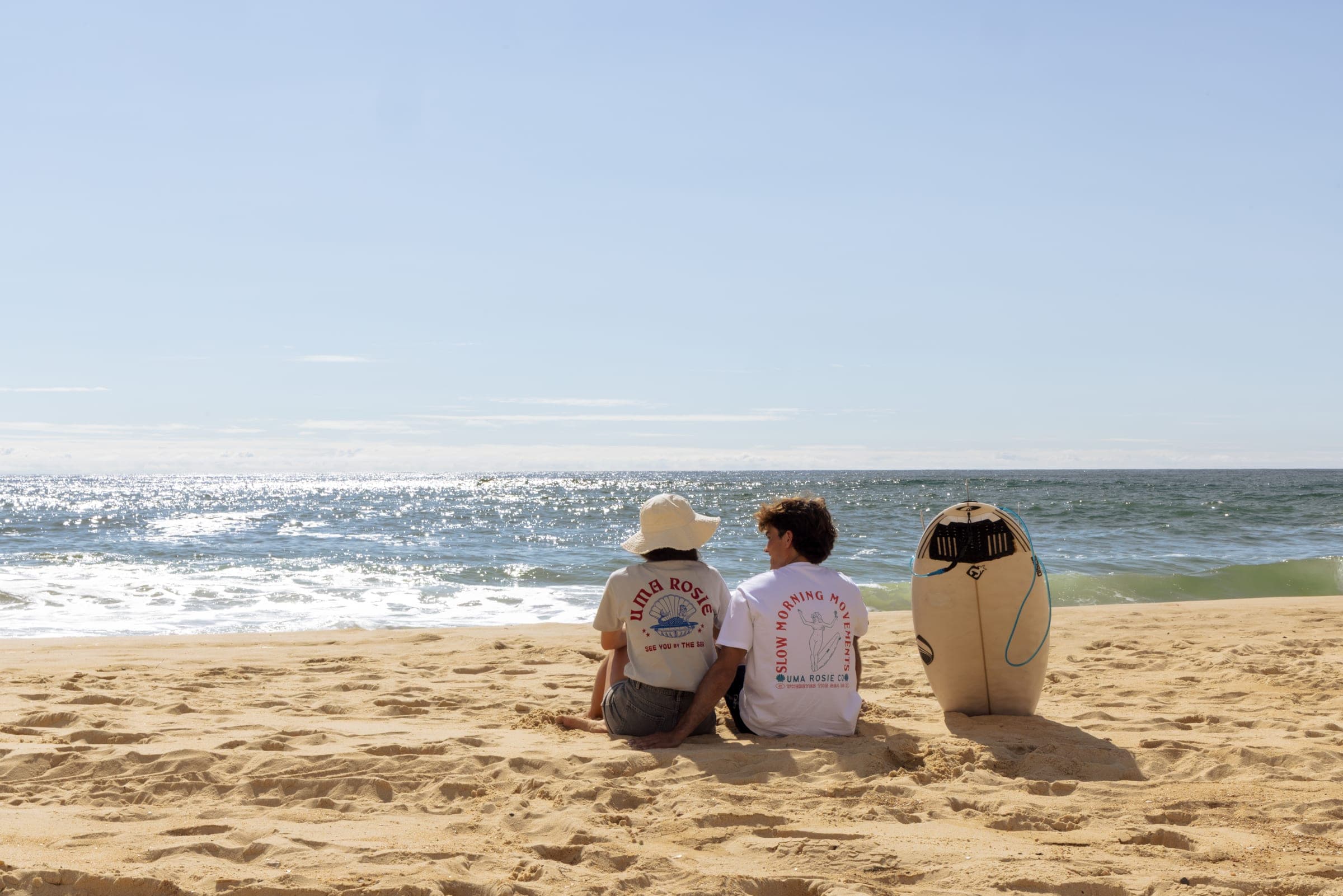 Deux personnes assises sur le sable devant leurs planches, face à l'océan.