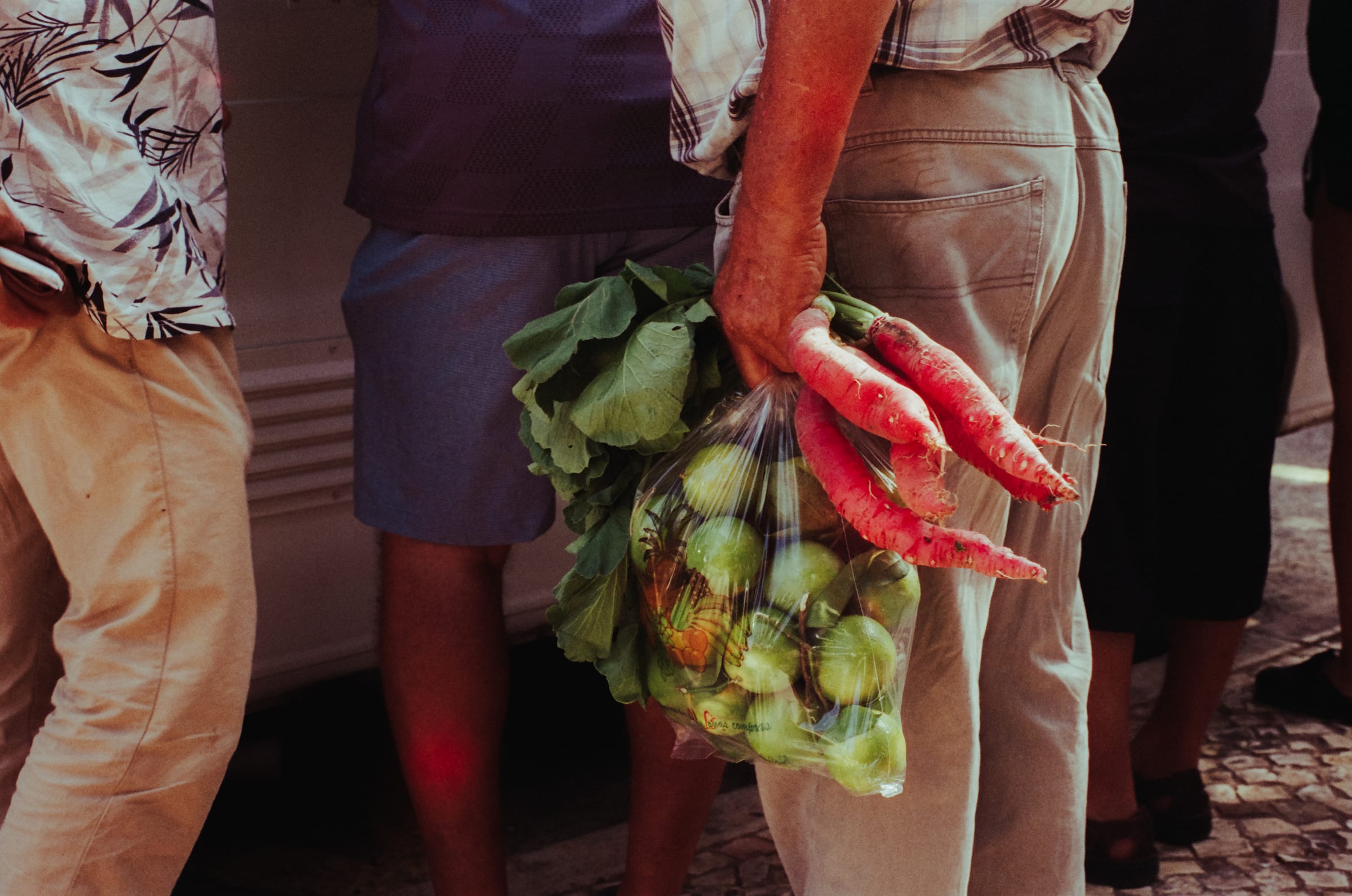 Un sac de légumes et de longs radis roses tenus dans le dos, entre les jambes des clients du marché.