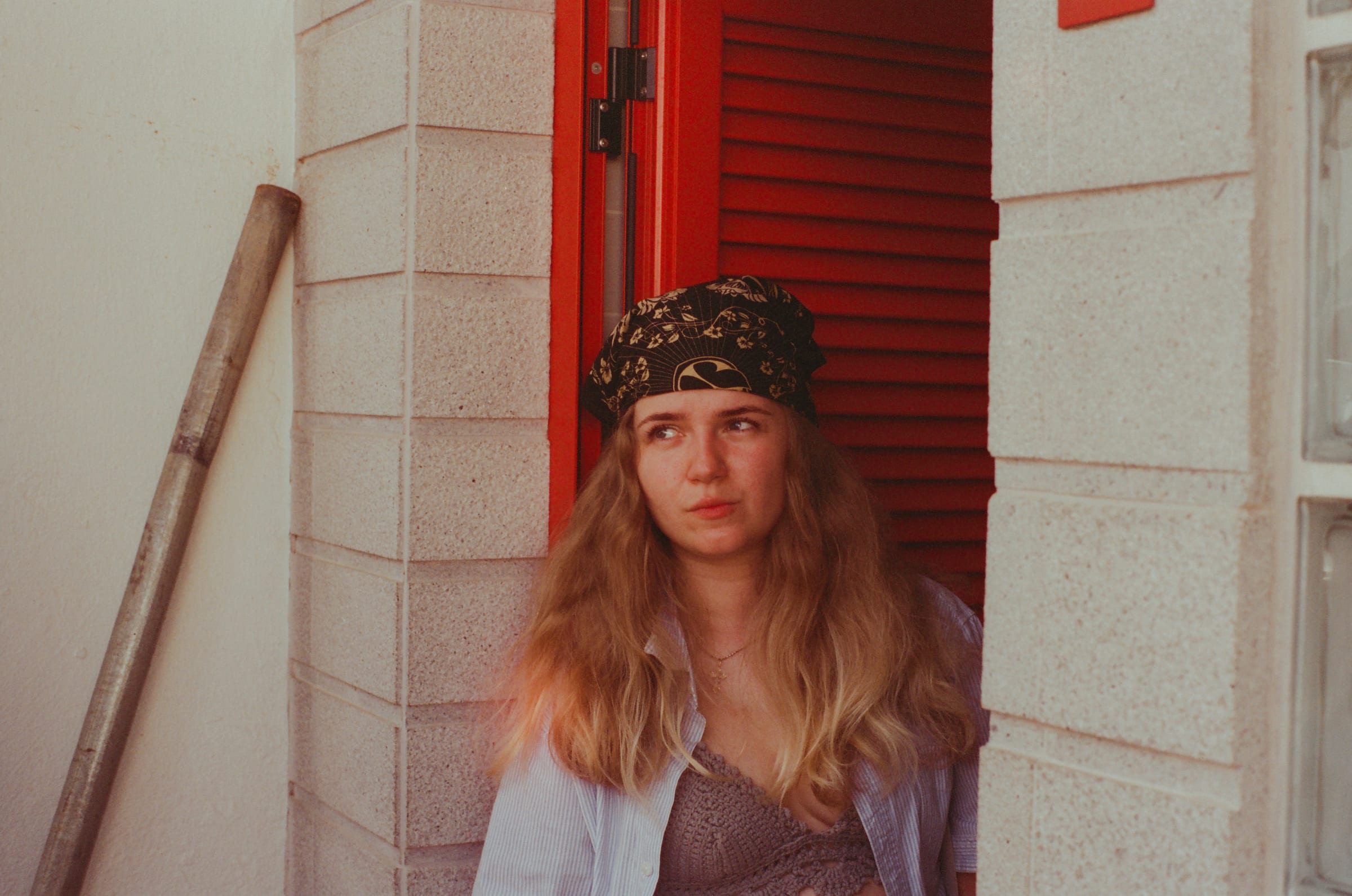 Dasha, bandana sur la tête, assise devant un volet rouge, regarde hors du cadre.