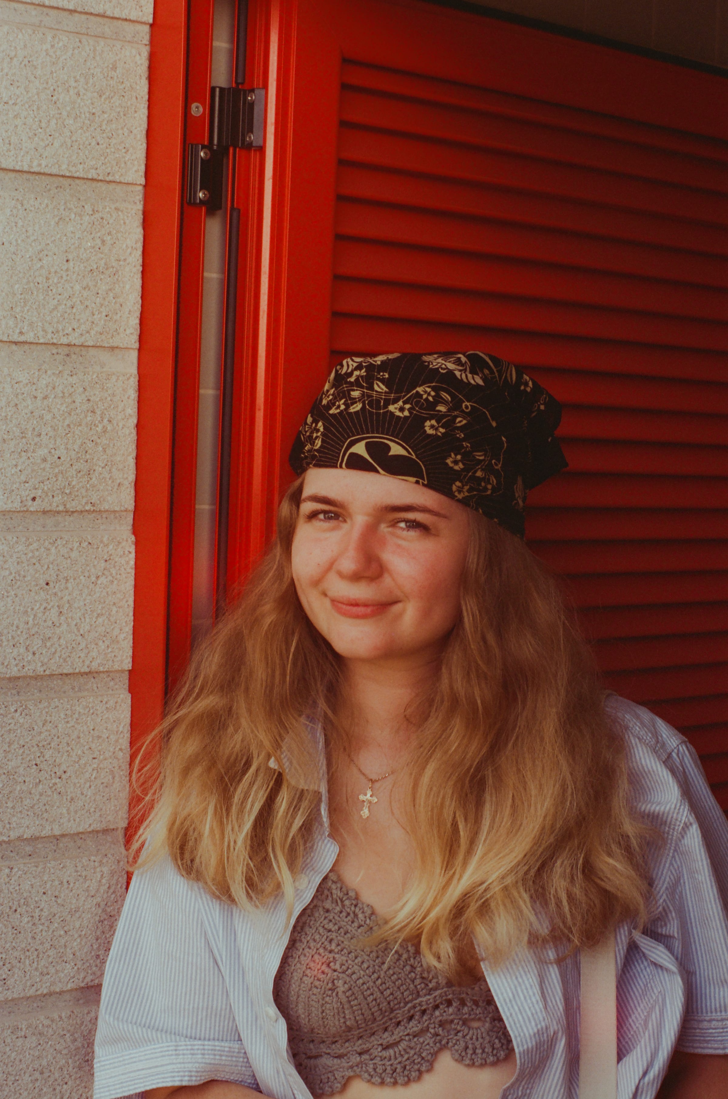 Dasha sourit, adossée au volet rouge.