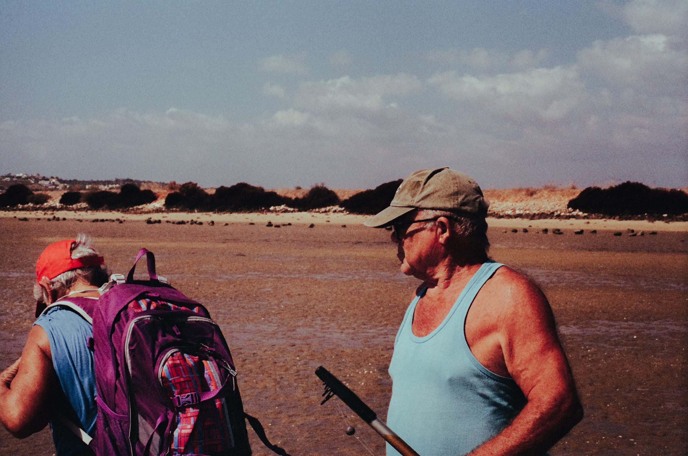 Deux pêcheurs sur le sable mouillé, l'un avec un sac à dos violet, l'autre une canne à la main.