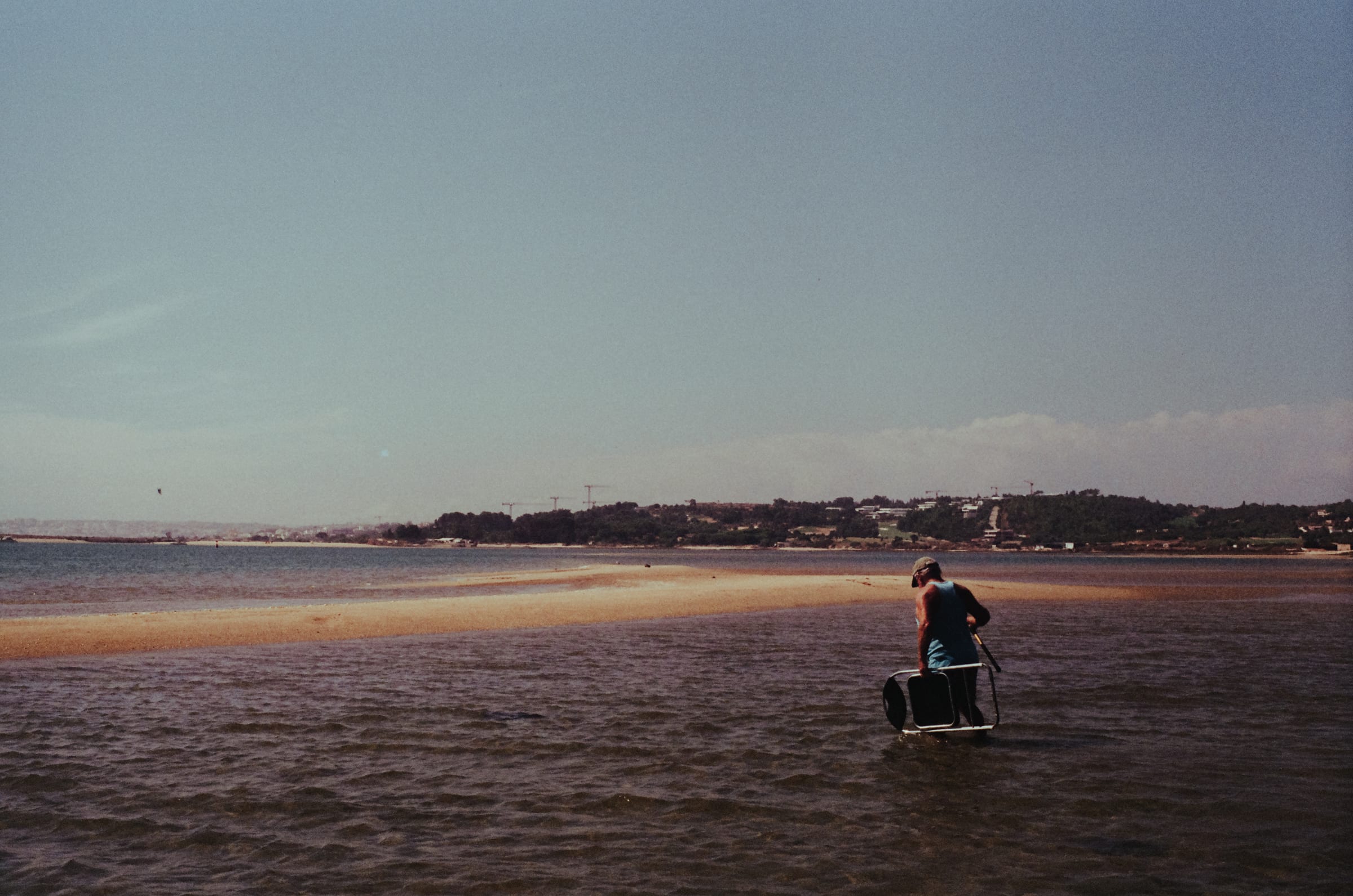 Un homme traverse le chenal à pied, une chaise pliante à la main, vers le banc de sable.