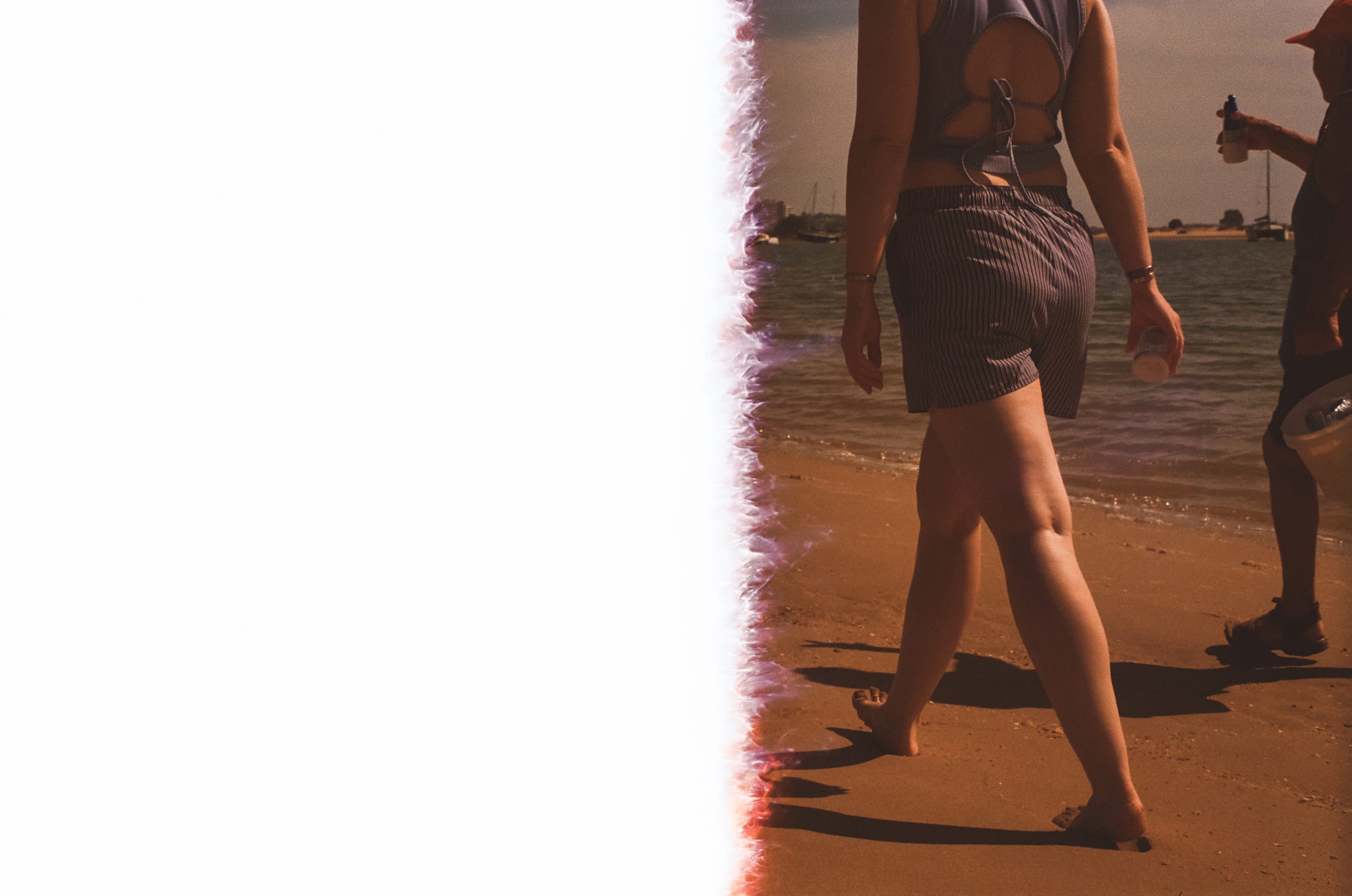 Une femme en short rayé marche pieds nus sur le sable, la moitié gauche de l'image brûlée par la pellicule.
